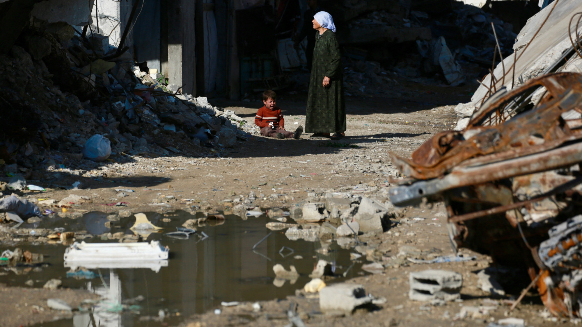 A Palestinian woman stands with a child next to the rubble of destroyed buildings in the Jabalia refugee camp, in the northern Gaza Strip on 24 December 2025 (AFP/Bashar Taleb)