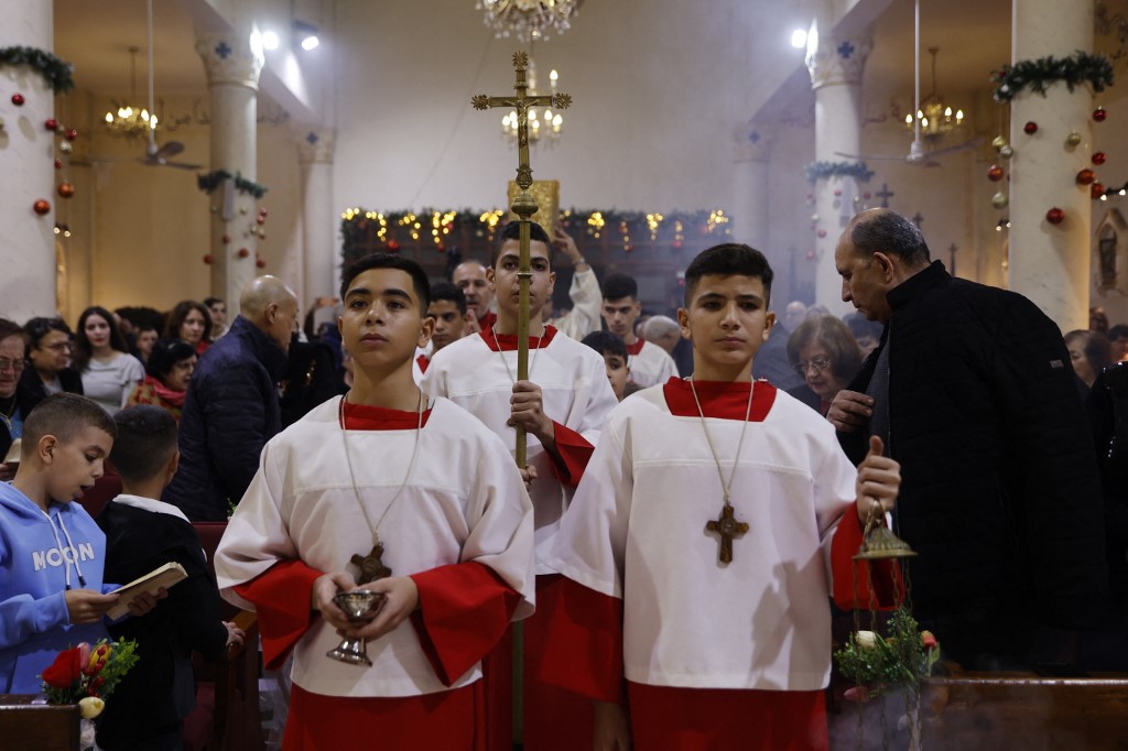 Alter servers and the cross bearer walk down the aisle during a Christmas mass celebrated with displaced worshippers at the Roman Catholic Church of the Holy Family in Gaza City on December 24, 2025.