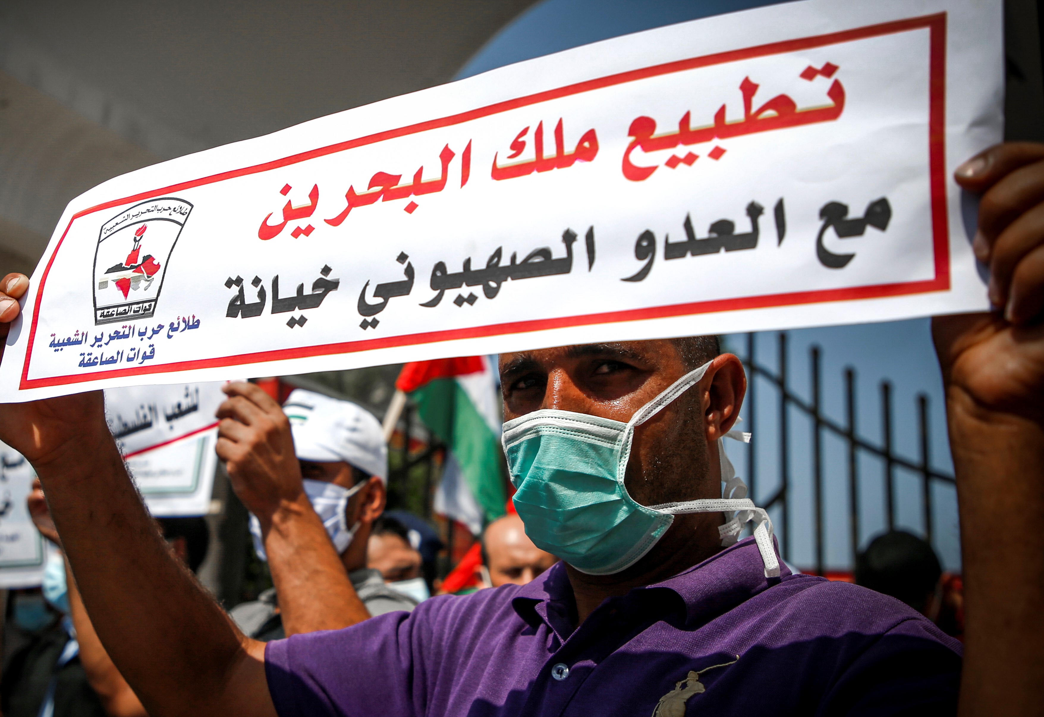 A demonstrator, mask-clad due to the COVID-19 coronavirus pandemic, stands holding a sign reading in Arabic 