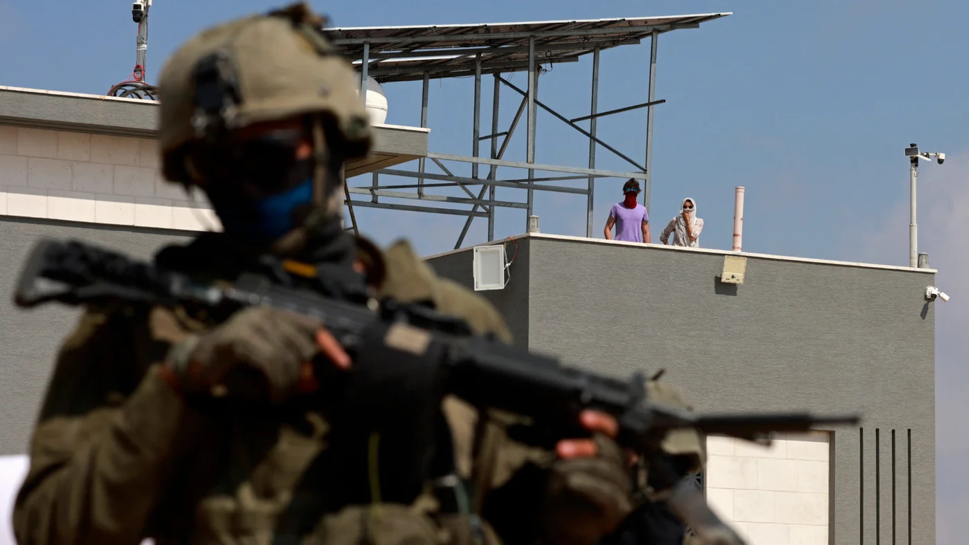 An Israeli soldier stands in front of a Palestinian house besieged by Israeli settlers in the village of Qusra, south of Nablus, in the occupied West Bank, on 14 August 2026 (Jaafar Ashtiyeh/AFP)
