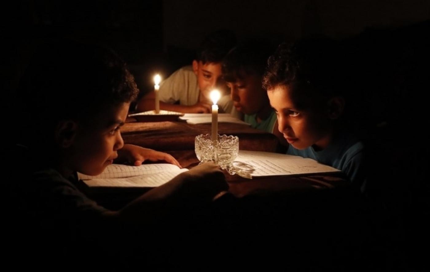 Des enfants palestiniens lisent des livres chez eux à la lueur de bougies en raison des pénuries d’électricité à Gaza, en juin&nbsp;2017 (AFP)