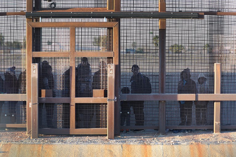 Migrants stand along the US/Mexico border wall on 12 February in El Paso, Texas (AFP)