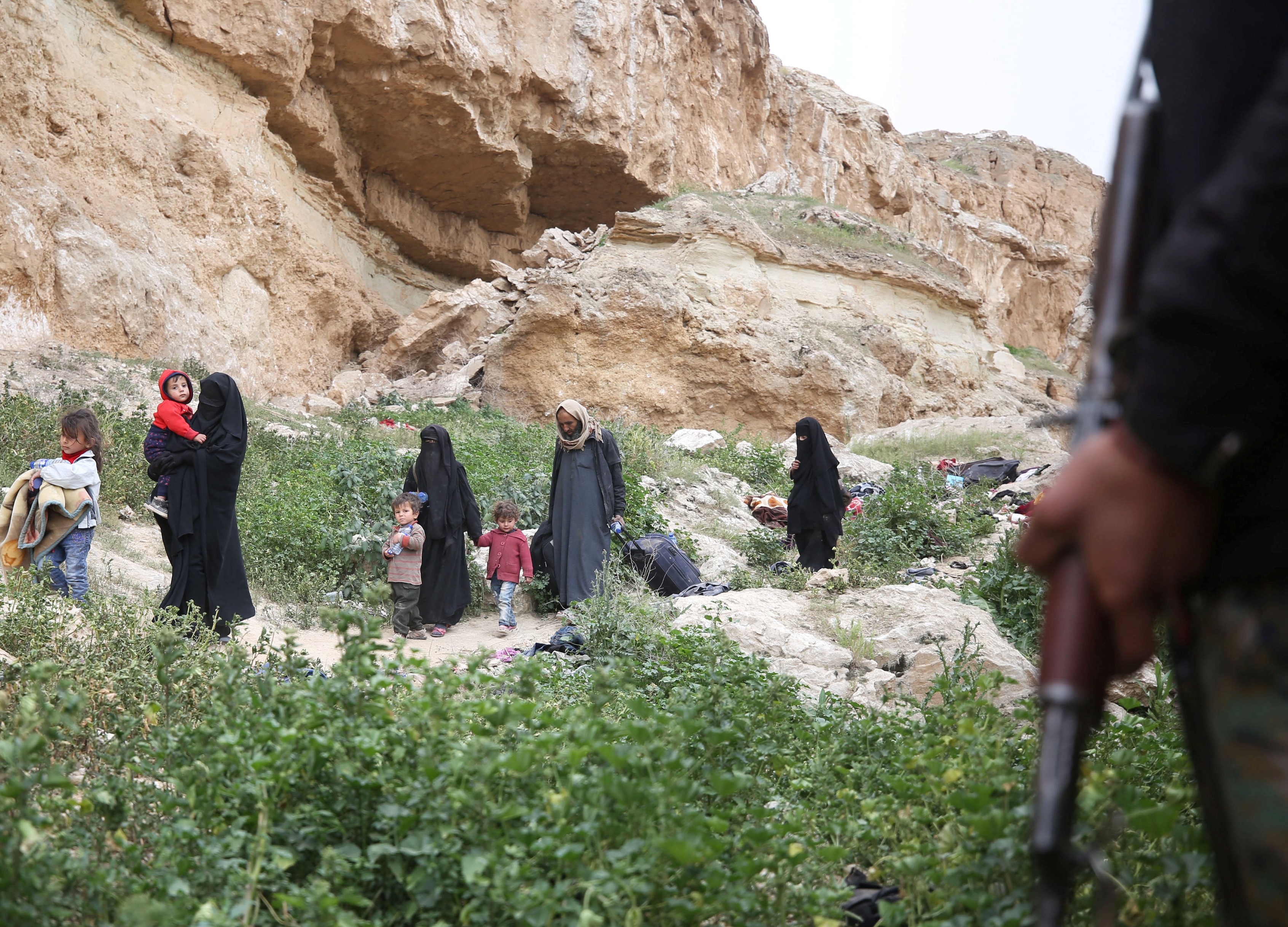 Islamic State fighters along with women and children walk as they surrendered in the village of Baghouz, Deir Al Zor province, Syria, 0n 14 March (REUTERS)