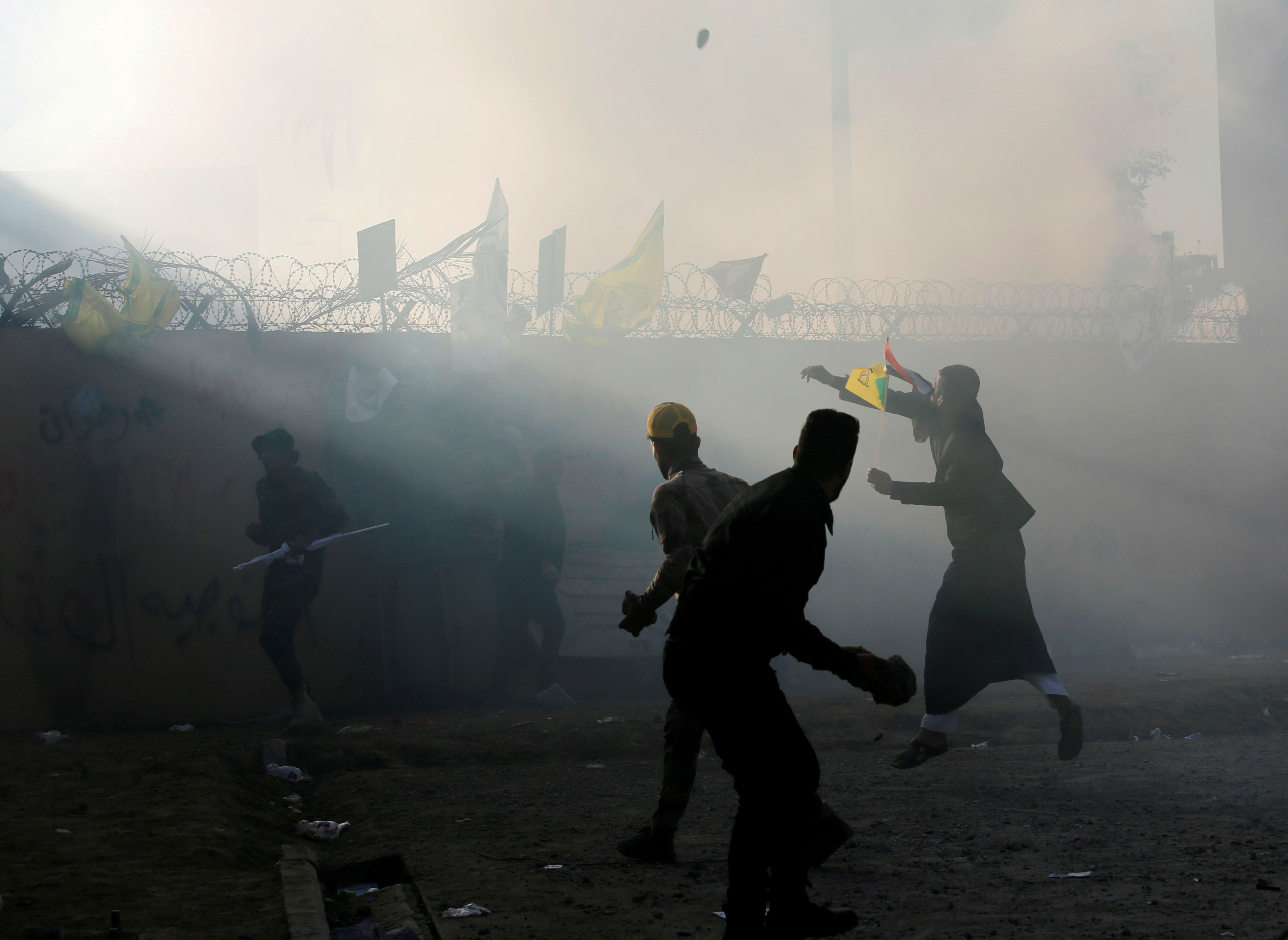 Protesters and militia fighters throw stones towards the US embassy during a protest to condemn air strikes on bases belonging to Hashd al-Shaabi (Reuters)