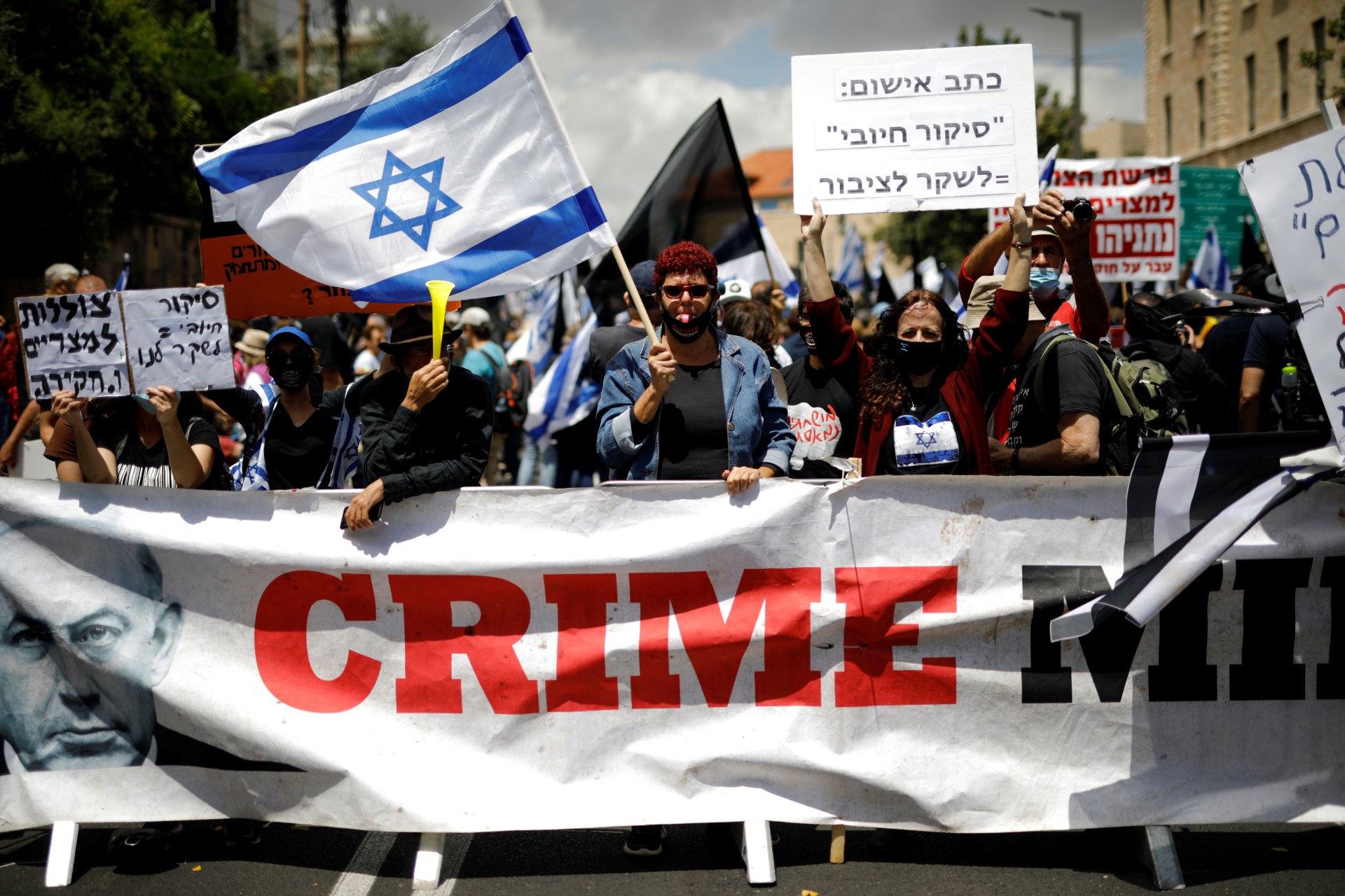 Protesters wave an Israeli flag and hold placards as they stand behind a banner reading, 