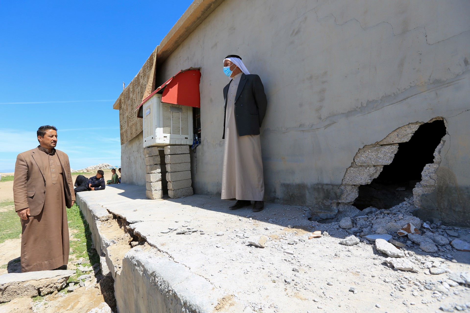 People stand next to a damaged house after a rocket attack on a military compound, at a village in Bashiqa region, Iraq, 15 April (Reuters)