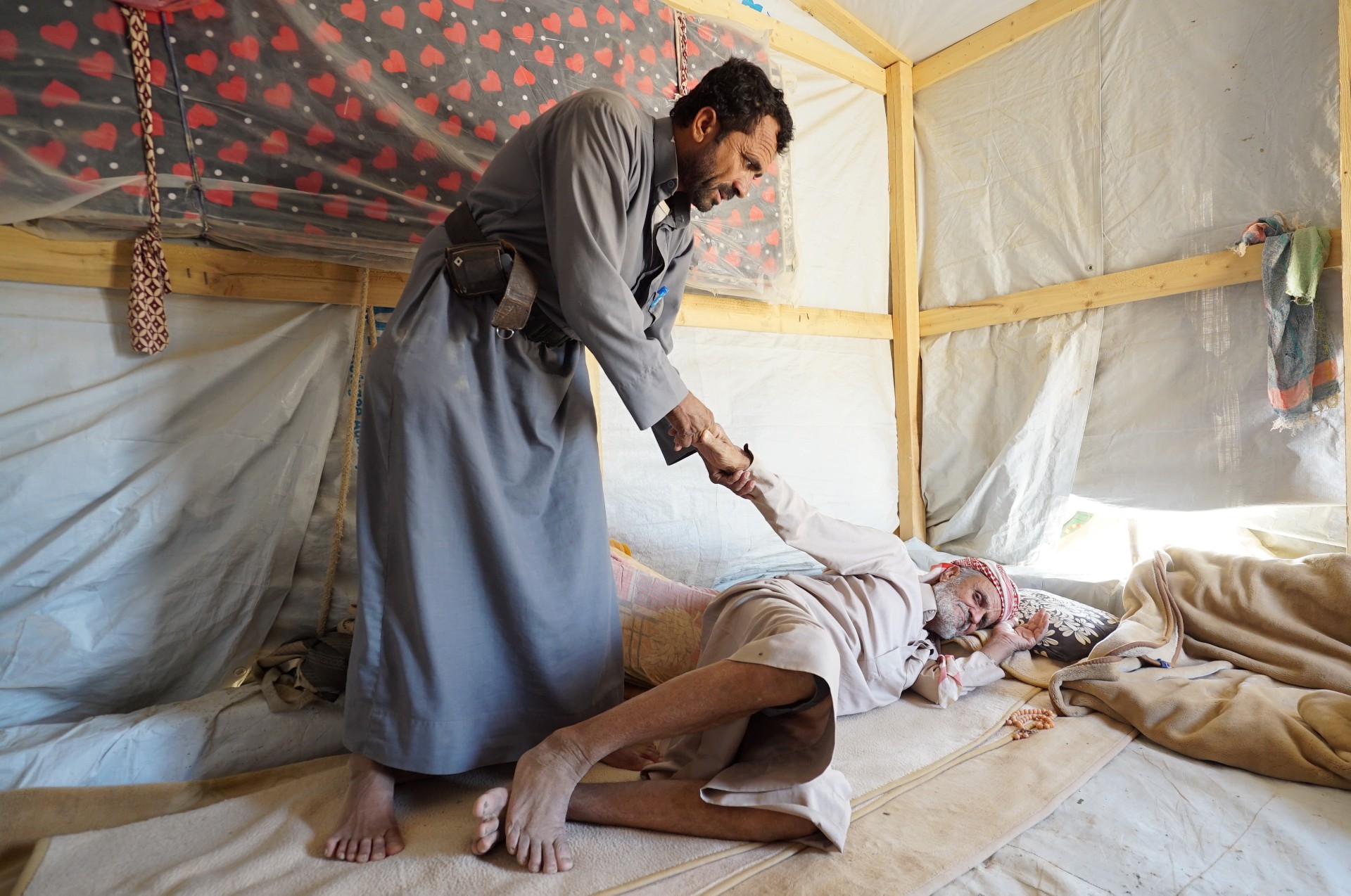 A man helps his father, who suffers from a spinal cord illness, to lie on a mattress at a camp for internally displaced persons (IDPs) in Marib, Yemen (Reuters)