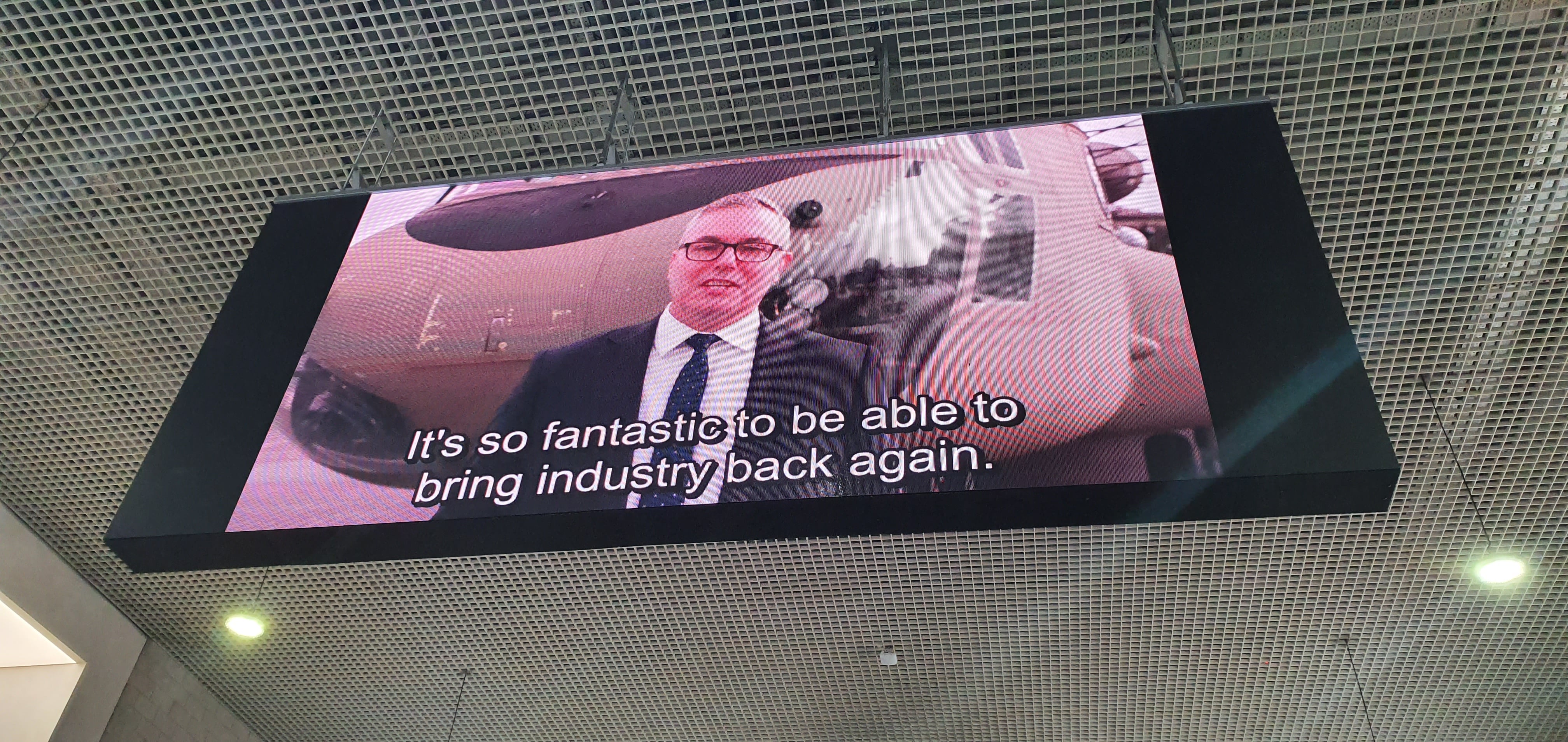 Attendees are greeted by a video playing on a big screen hanging from the ceiling