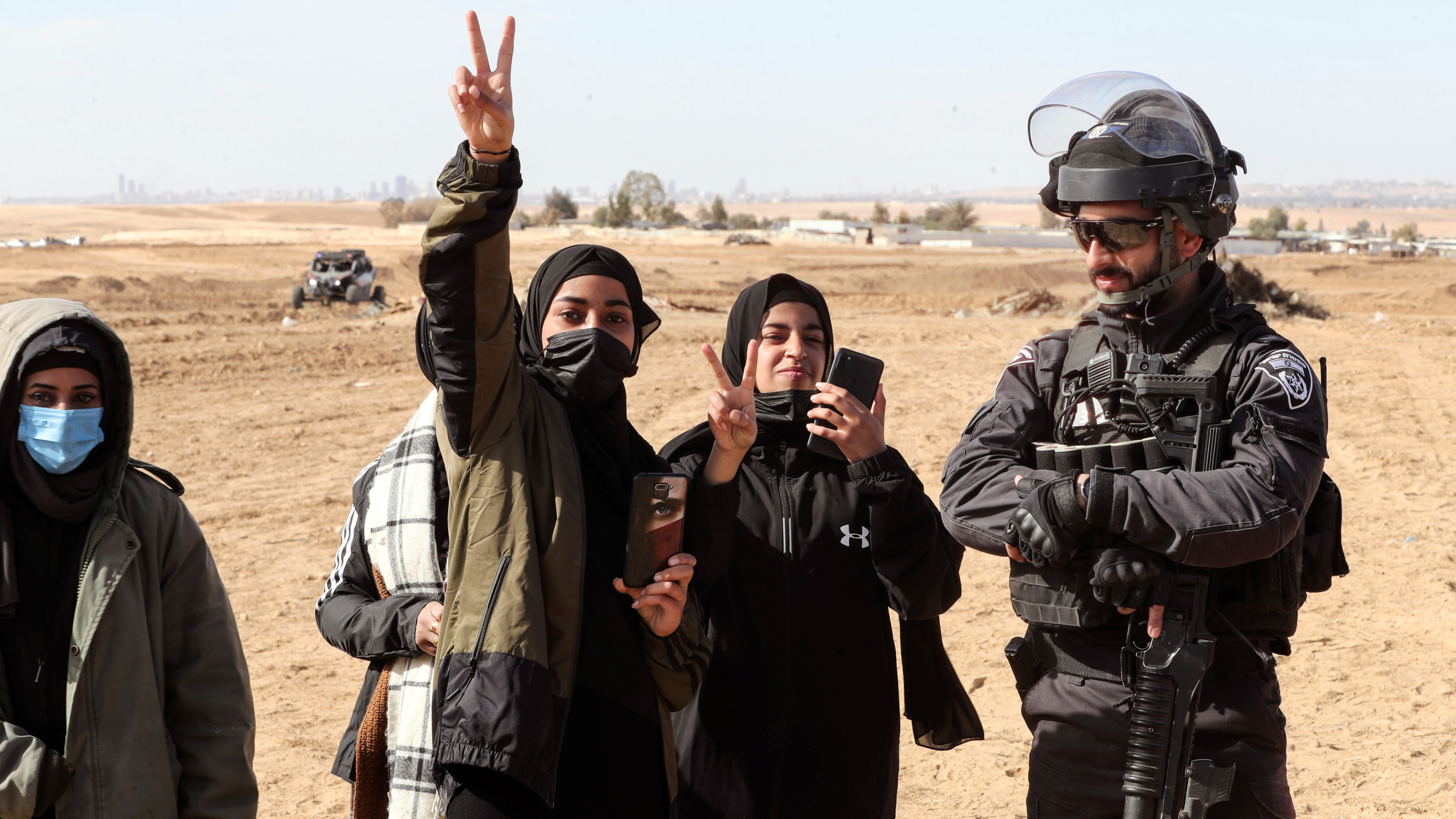 Palestinian women gesture as they stand by an Israeli policeman during a protest against government expulsions in the village of Sawe al-Atrash in the Negev on 12 January 2022 (Reuters)