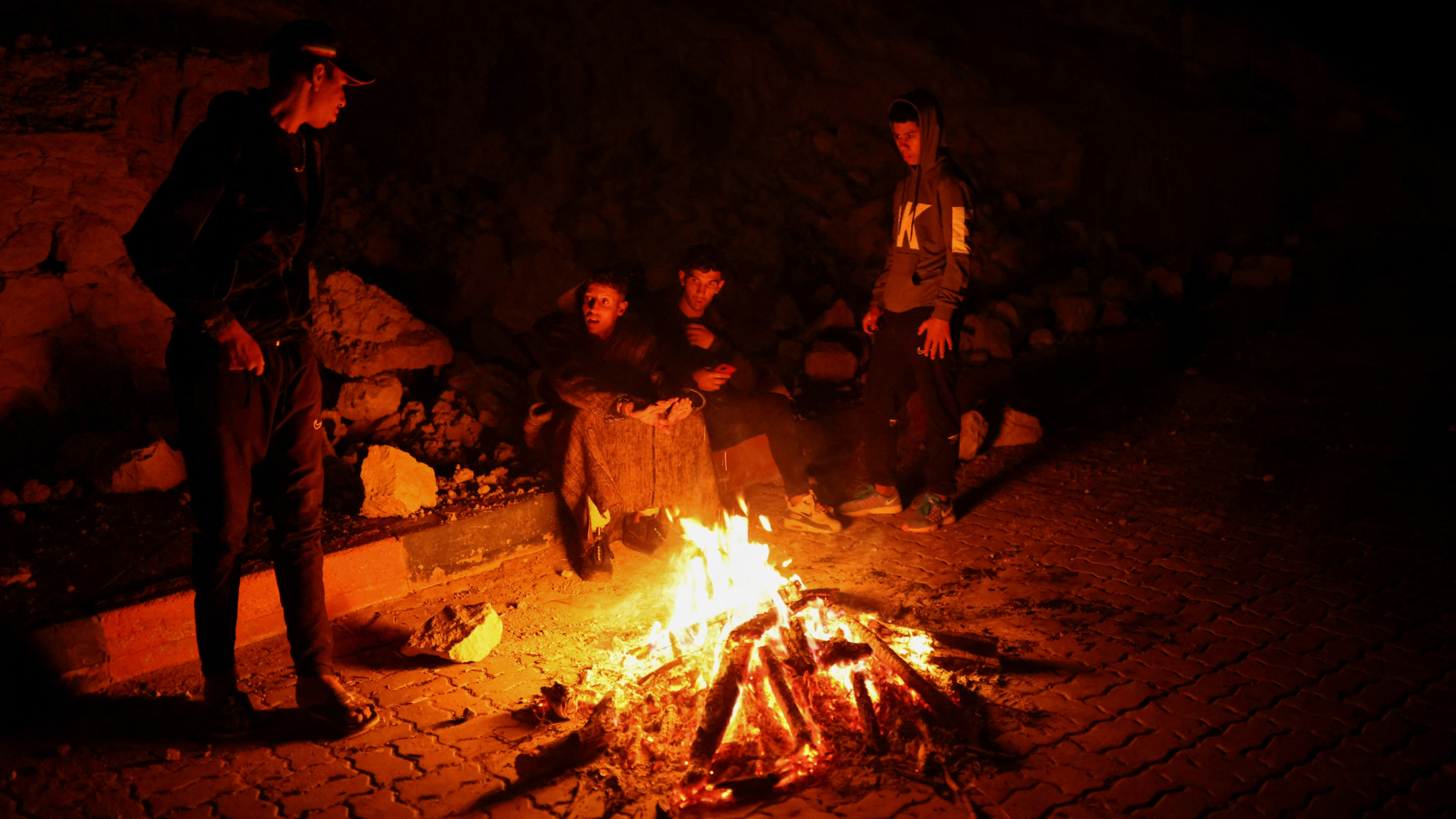 Des habitants sont assis autour d’un feu à la suite du séisme dans le village de Moulay Brahim, le 9 septembre 2023 dans la province d’Al Haouz (Reuters)