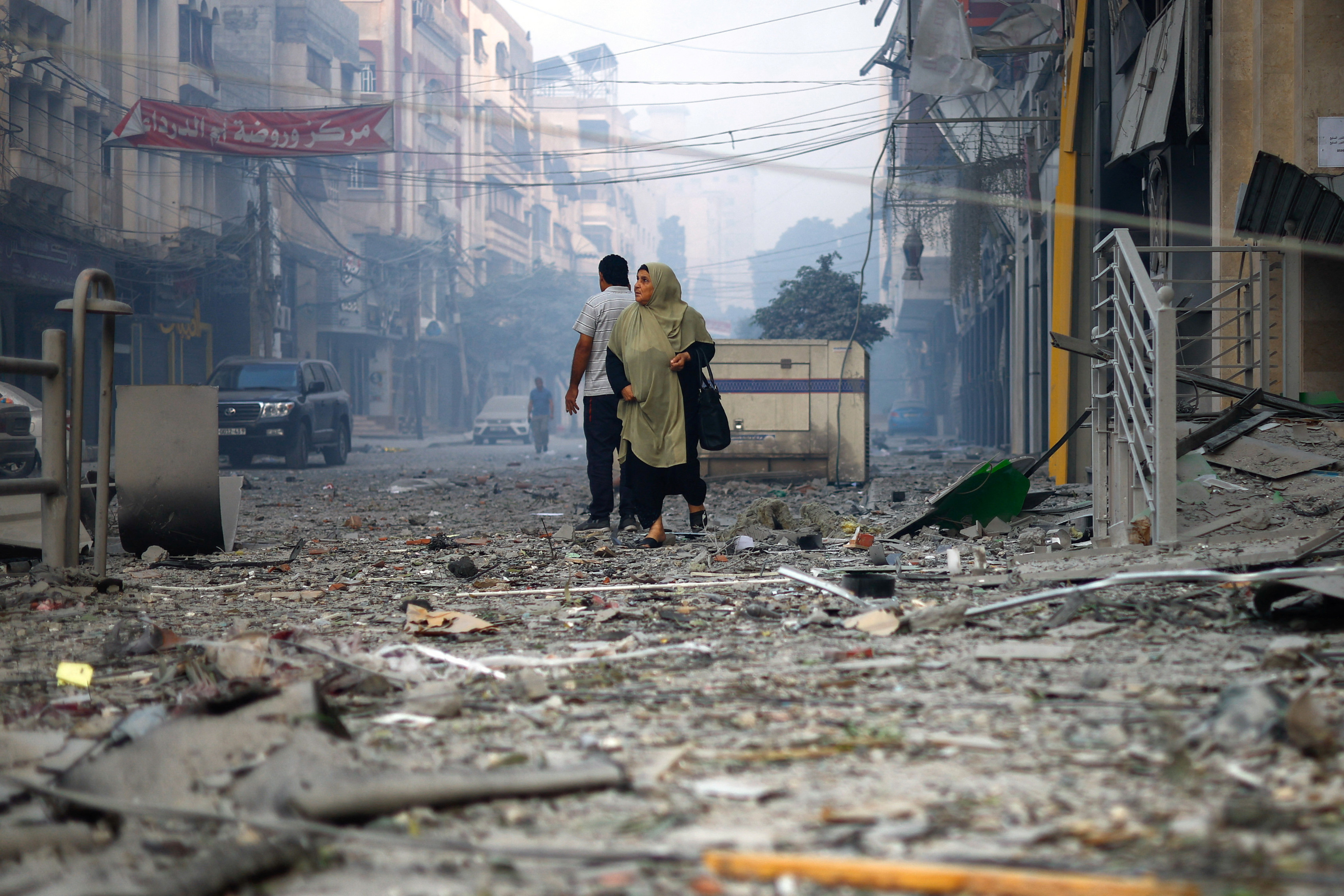 A Palestinian woman looks on as she walks on a debris-strewn street near the Watan Tower, which was destroyed in Israeli strikes, in Gaza City 8 October 2023 (Reuters)