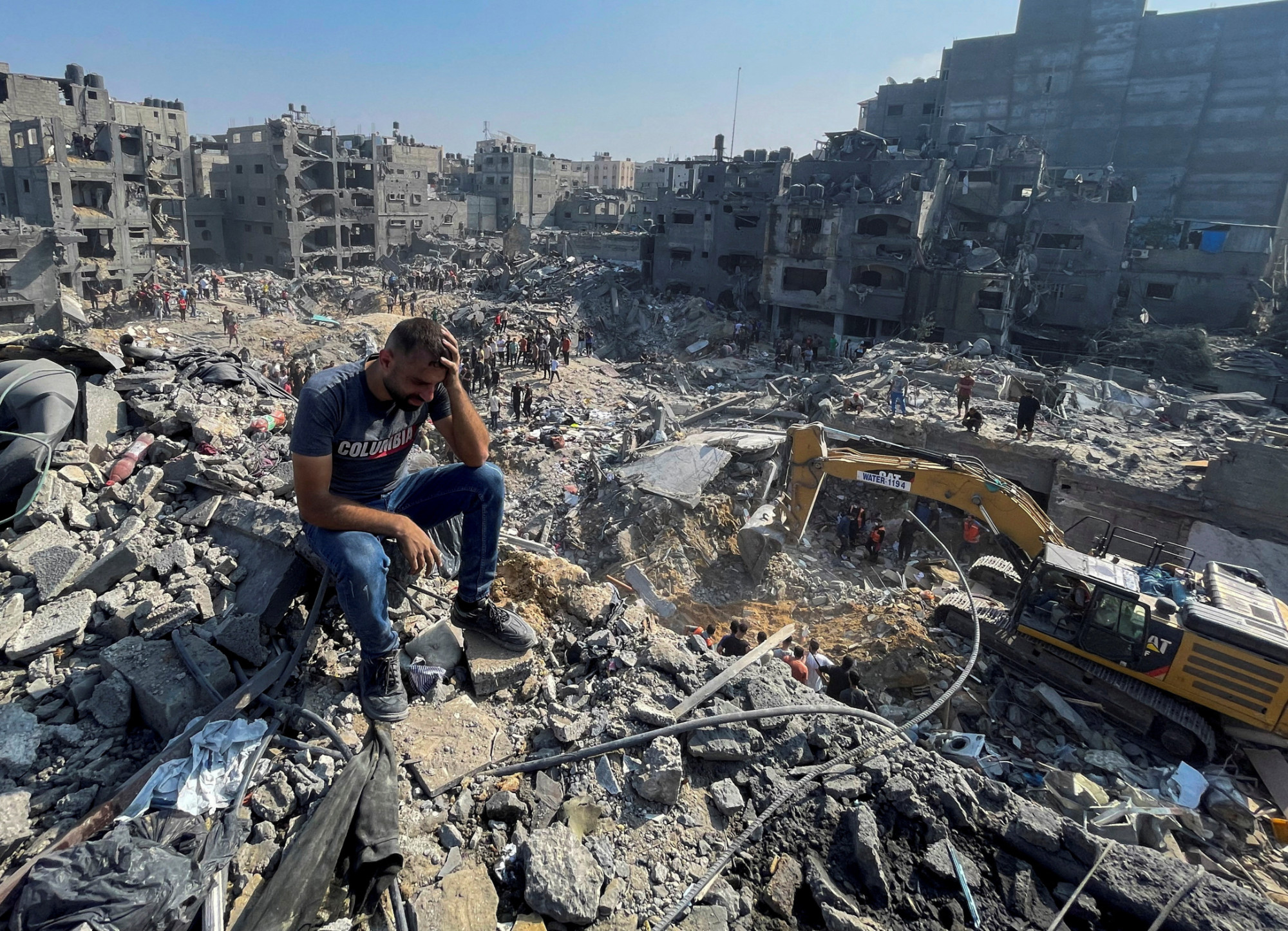 A man sits on the rubble as others wander among debris of buildings that were targeted by Israeli airstrikes in Jabaliya refugee camp, northern Gaza Strip,1 November 2023 (AP)