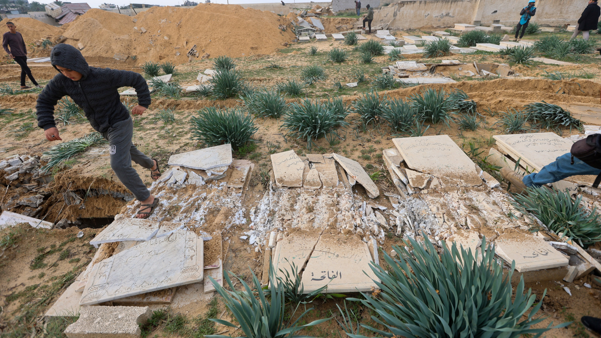 Palestinians check damaged graves at a cemetery following an Israeli raid in Khan Younis in the southern Gaza Strip 17 January 2024 (Ahmed Zakot/Reuters)