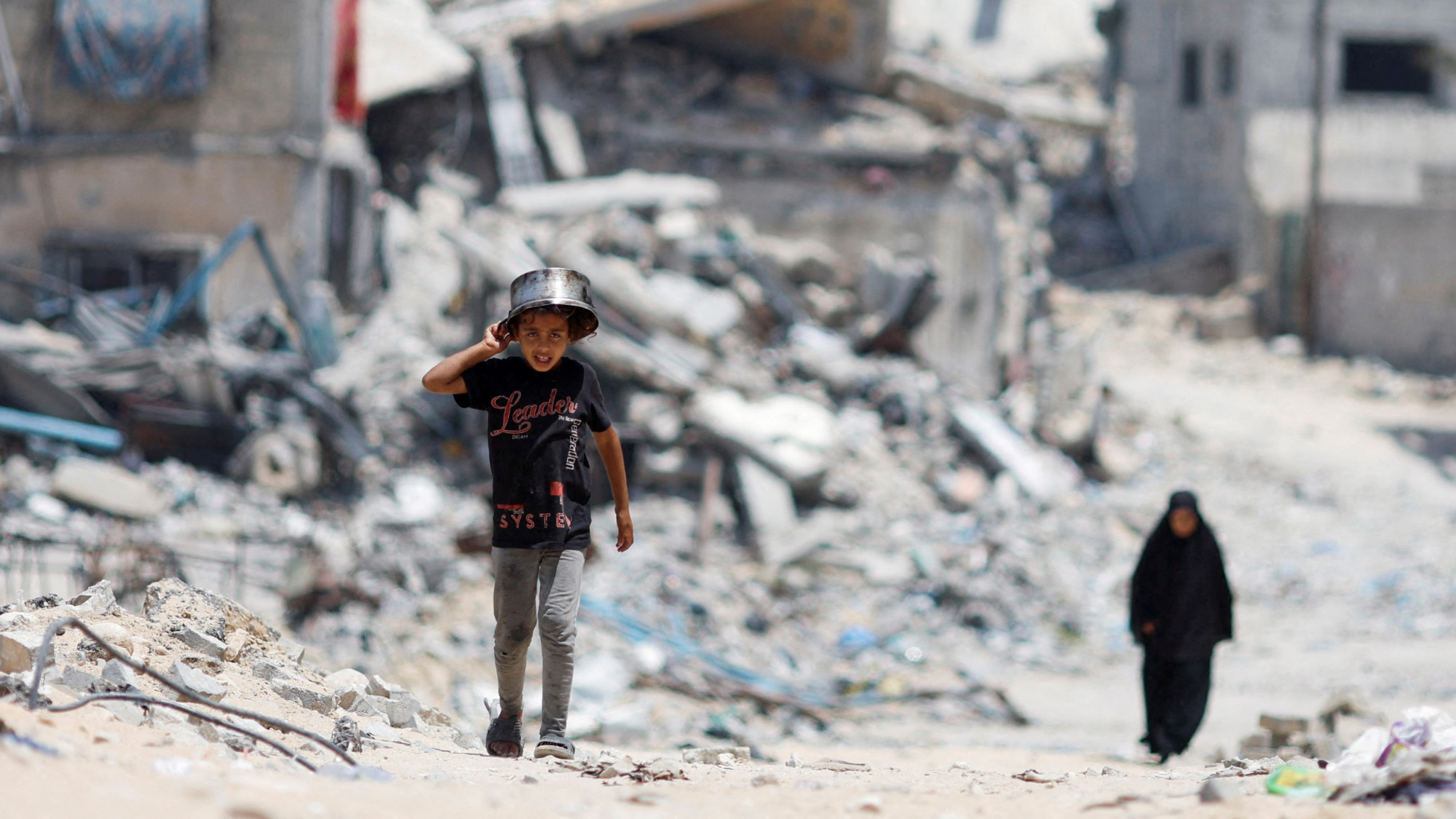 Palestinians walk by houses destroyed in an Israeli strike in Khan Younis, in the southern Gaza Strip, 22 May 2024 (Reuters/Mohammed Salem)
