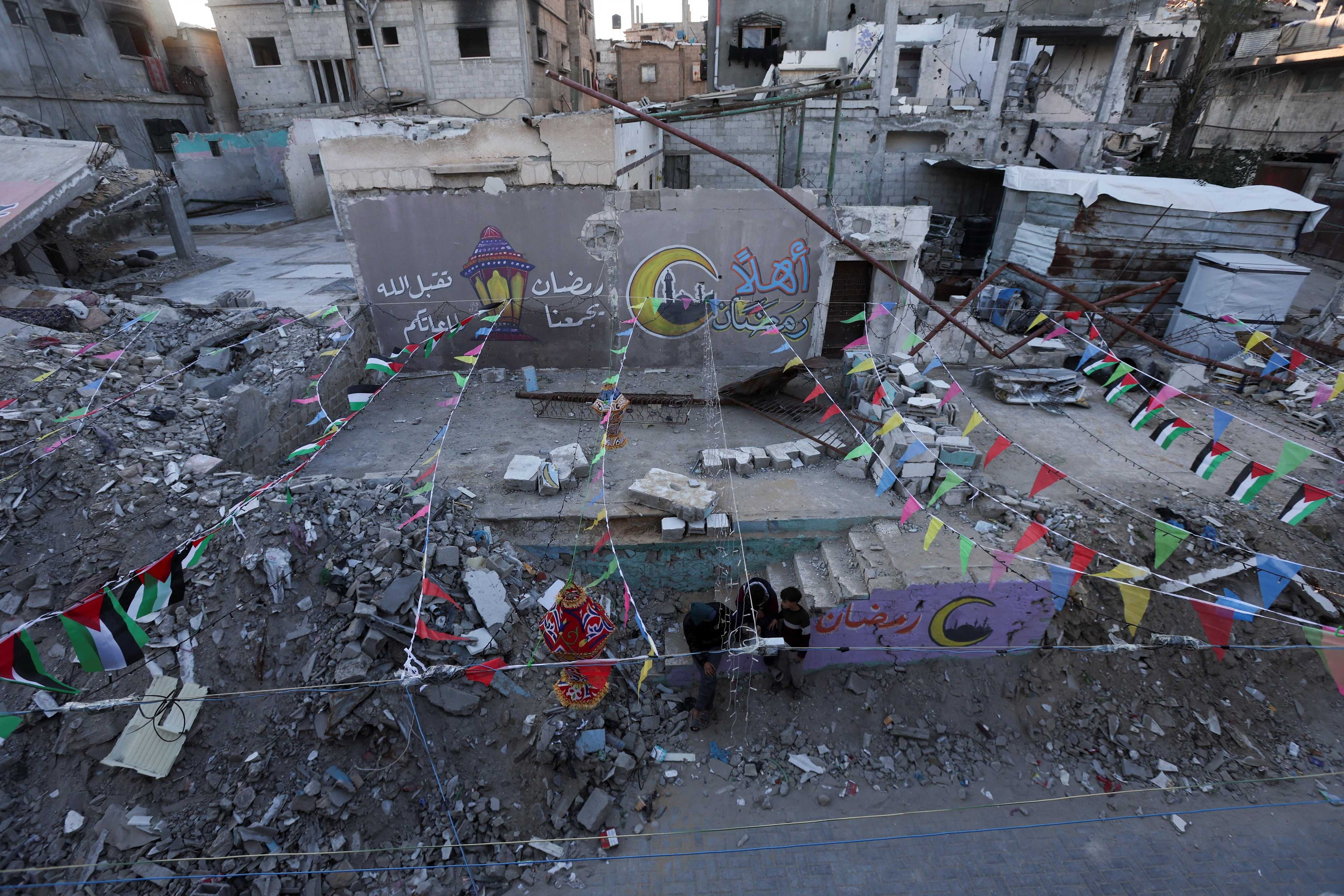 Palestinians gather near graffiti and the rubble of buildings, ahead of the holy fasting month of Ramadan, in Khan Younis, in the southern&nbsp;Gaza&nbsp;Strip, February 27, 2025. (REUTERS/Ramadan Abed)