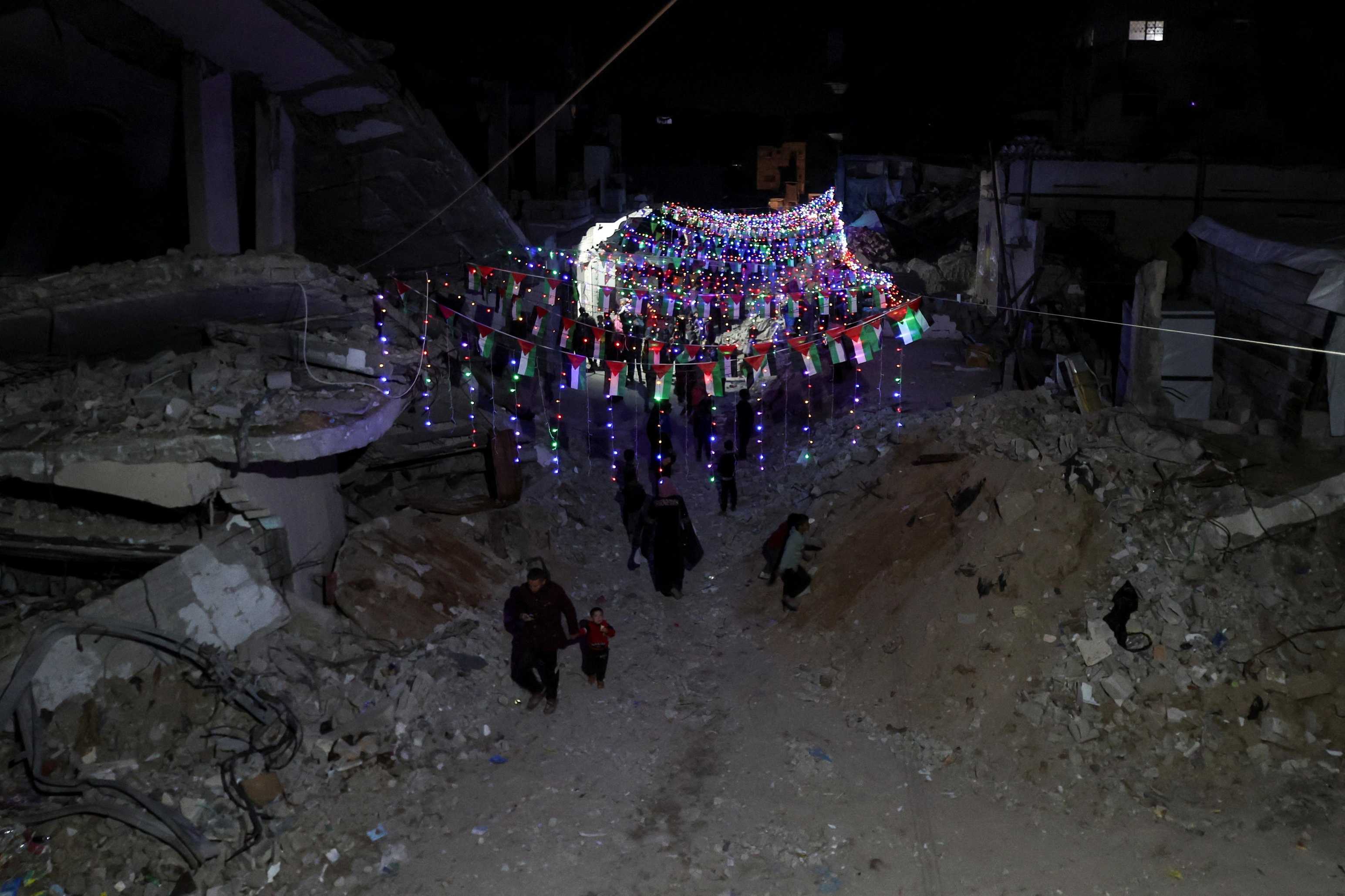 Palestinians walk under decorative lights and near the rubble of buildings, ahead of the holy fasting month of Ramadan, in Khan Younis, in the southern&nbsp;Gaza&nbsp;Strip, February 27, 2025. (REUTERS/Ramadan Abed)