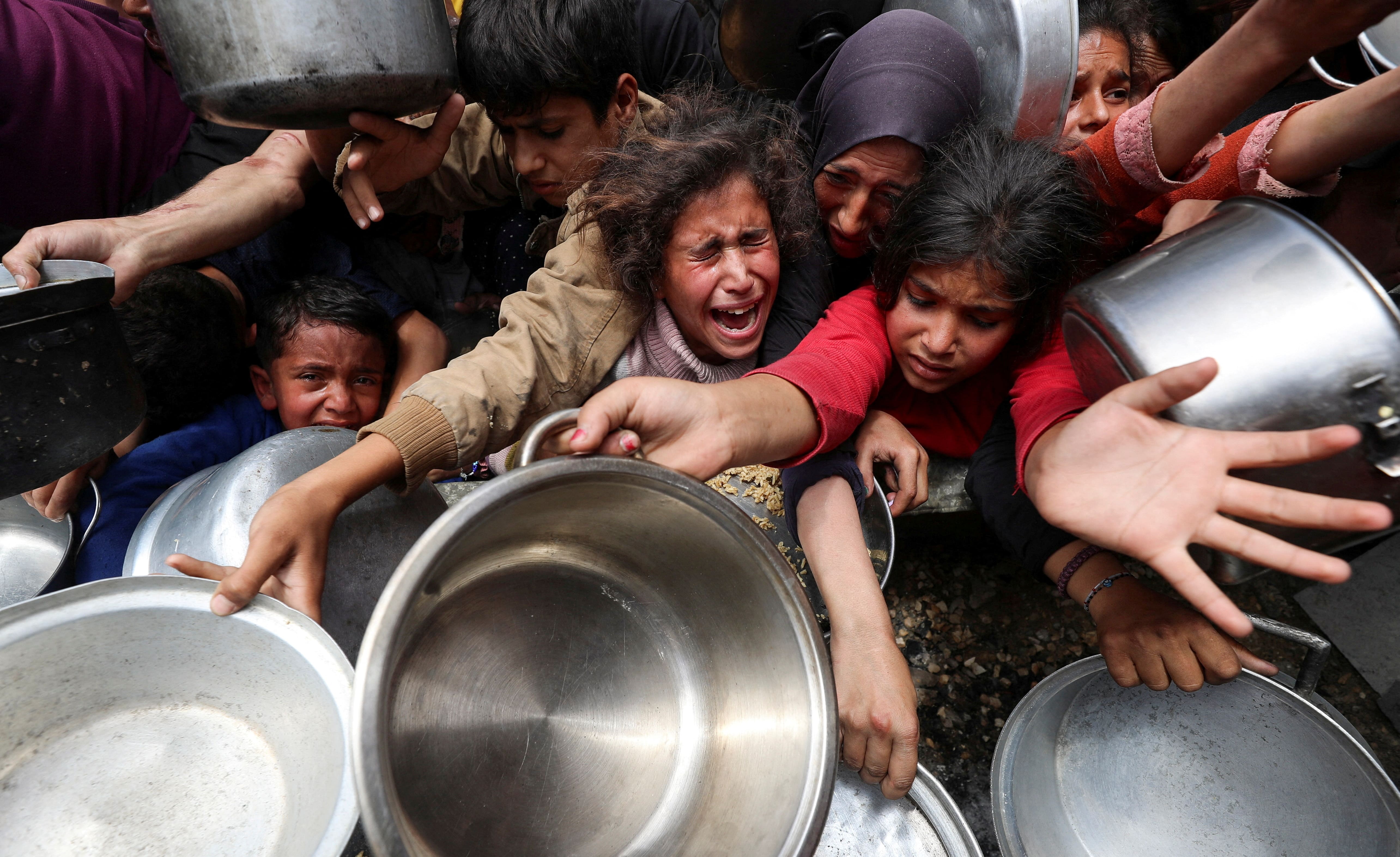 Palestinians wait to receive food cooked by a charity kitchen in Jabalia, north Gaza, on 14 May, 2025 (Reuters/Mahmoud Issa)