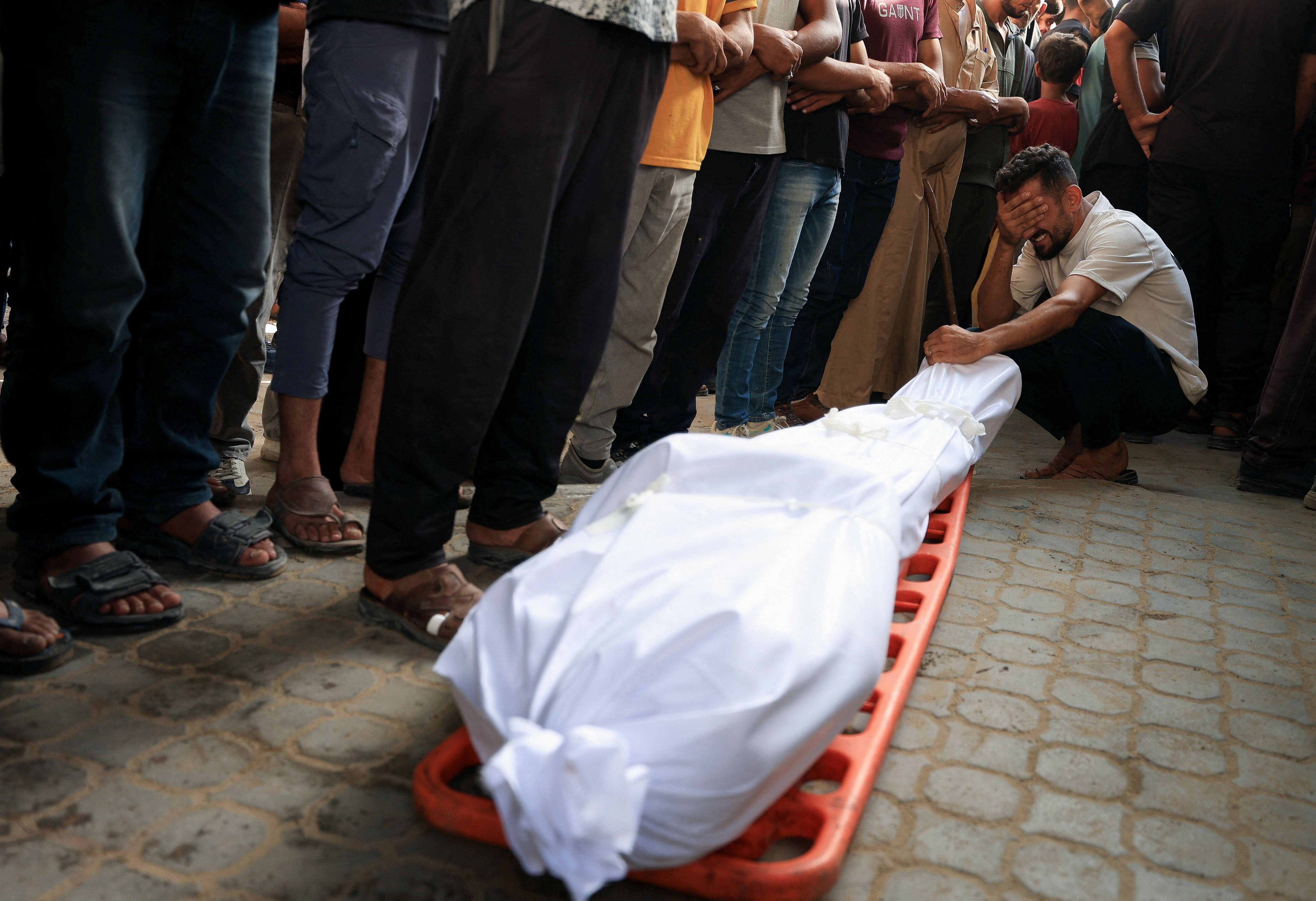 A mourner reacts next to a body during the funeral of Palestinians, who were killed by Israeli fire while trying to receive aid on Wednesday, and Palestinians who were killed in an overnight Israeli airstrike on a house, according to medics, at Al-Shifa Hospital, in Gaza City, July 31, 2025.