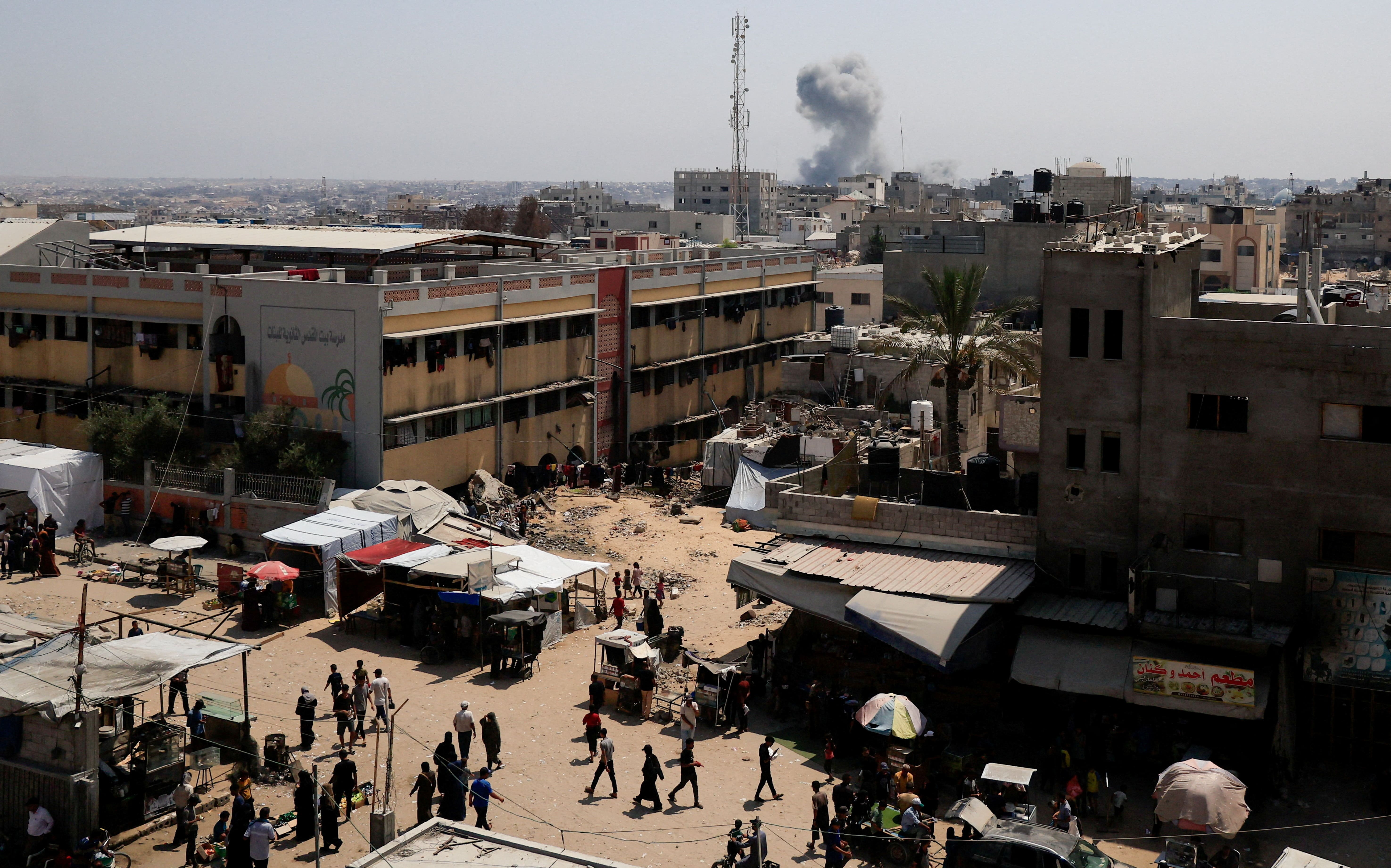 Palestinians walk as smoke rises in the distance, following an Israeli strike, in Khan Younis in the southern Gaza Strip, August 14, 2025. REUTERS