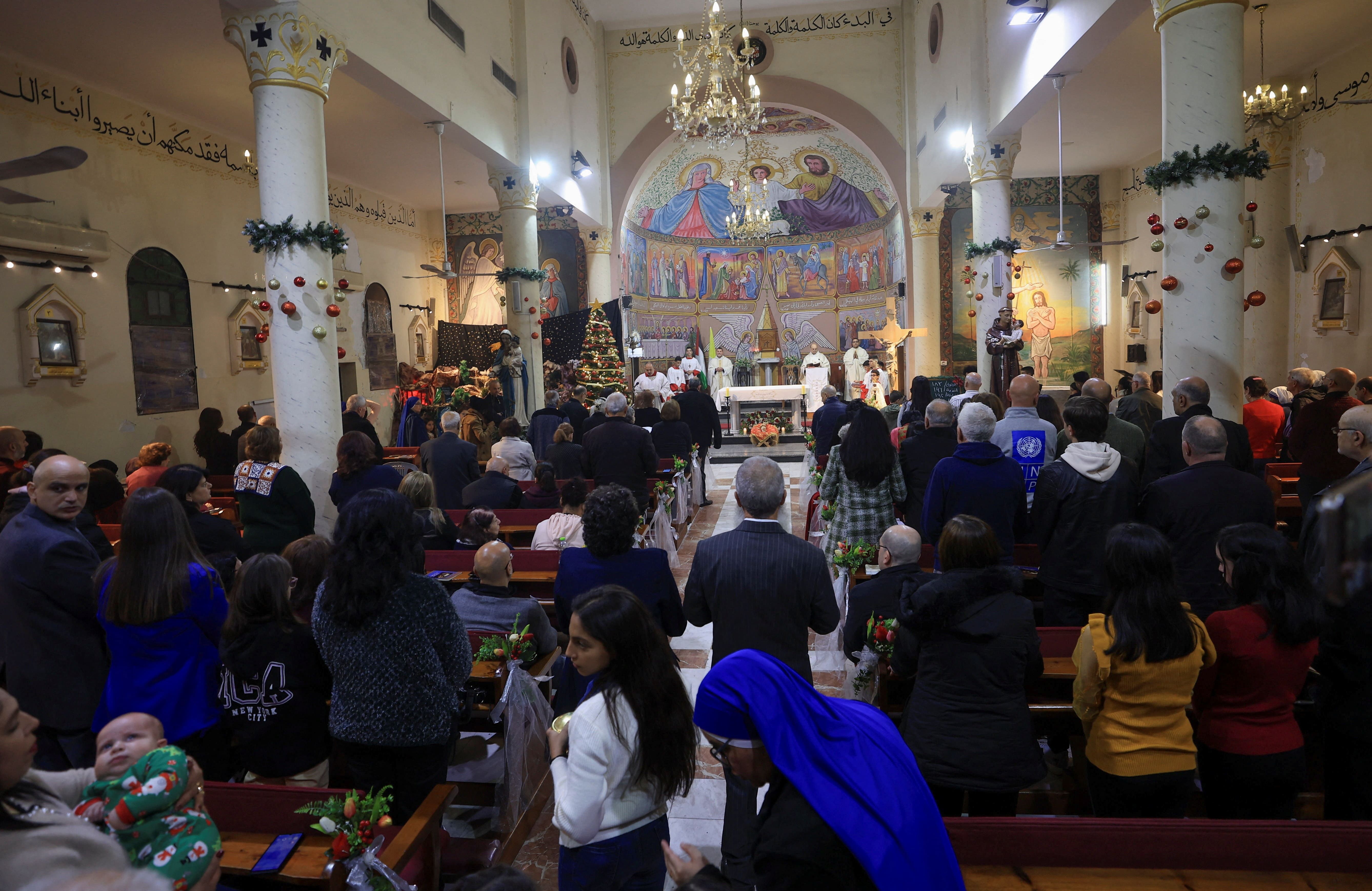 Alter servers and the cross bearer walk down the aisle during a Christmas mass celebrated with displaced worshippers at the Roman Catholic Church of the Holy Family in Gaza City on December 24, 2025.