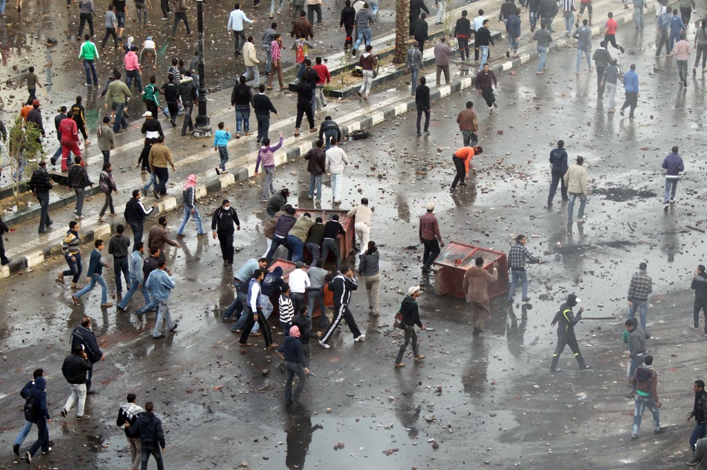 Protesters in Suez, some using upturned garbage skips for cover, call for the fall of Hosni Mubarak on 27 January 2011 (AFP)