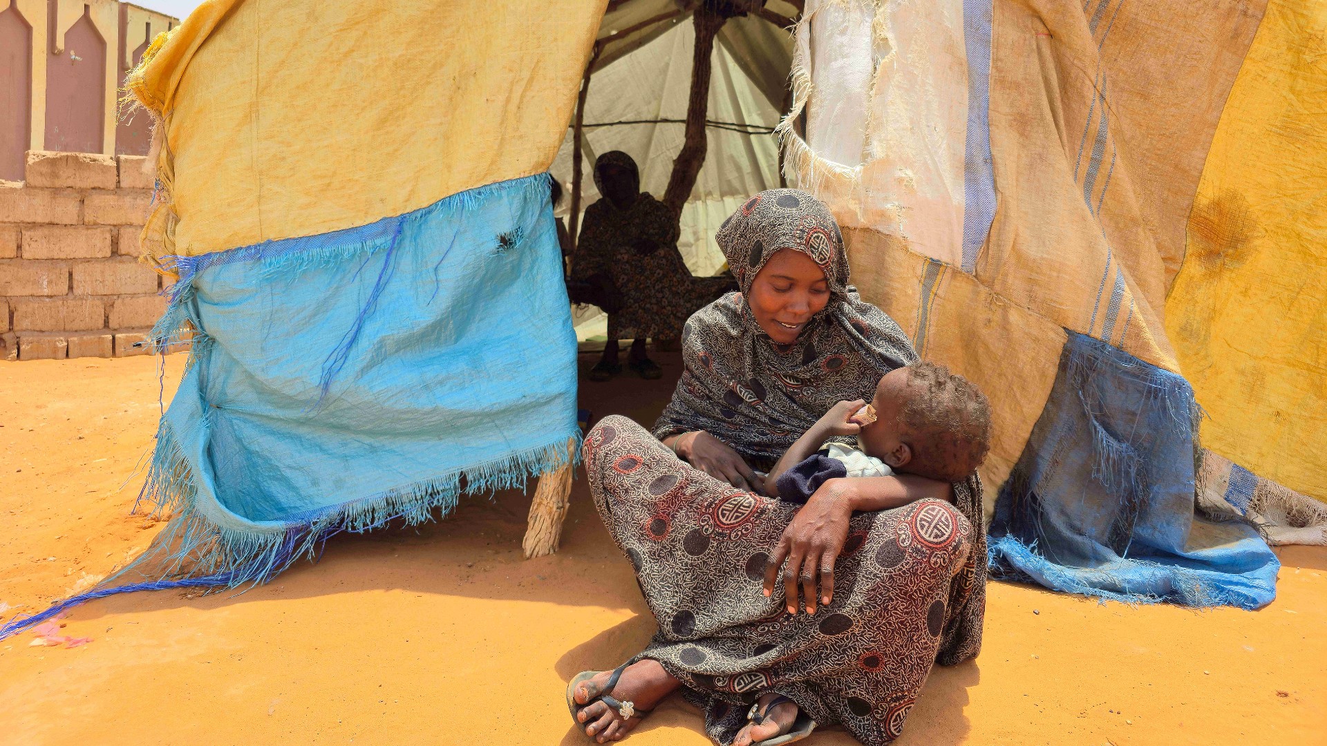 A Sudanese woman sits with her child in al-Rahmaniyah camp for displaced people, near the city of El-Obeid in the southern Kordofan region, on June 25, 2026. 