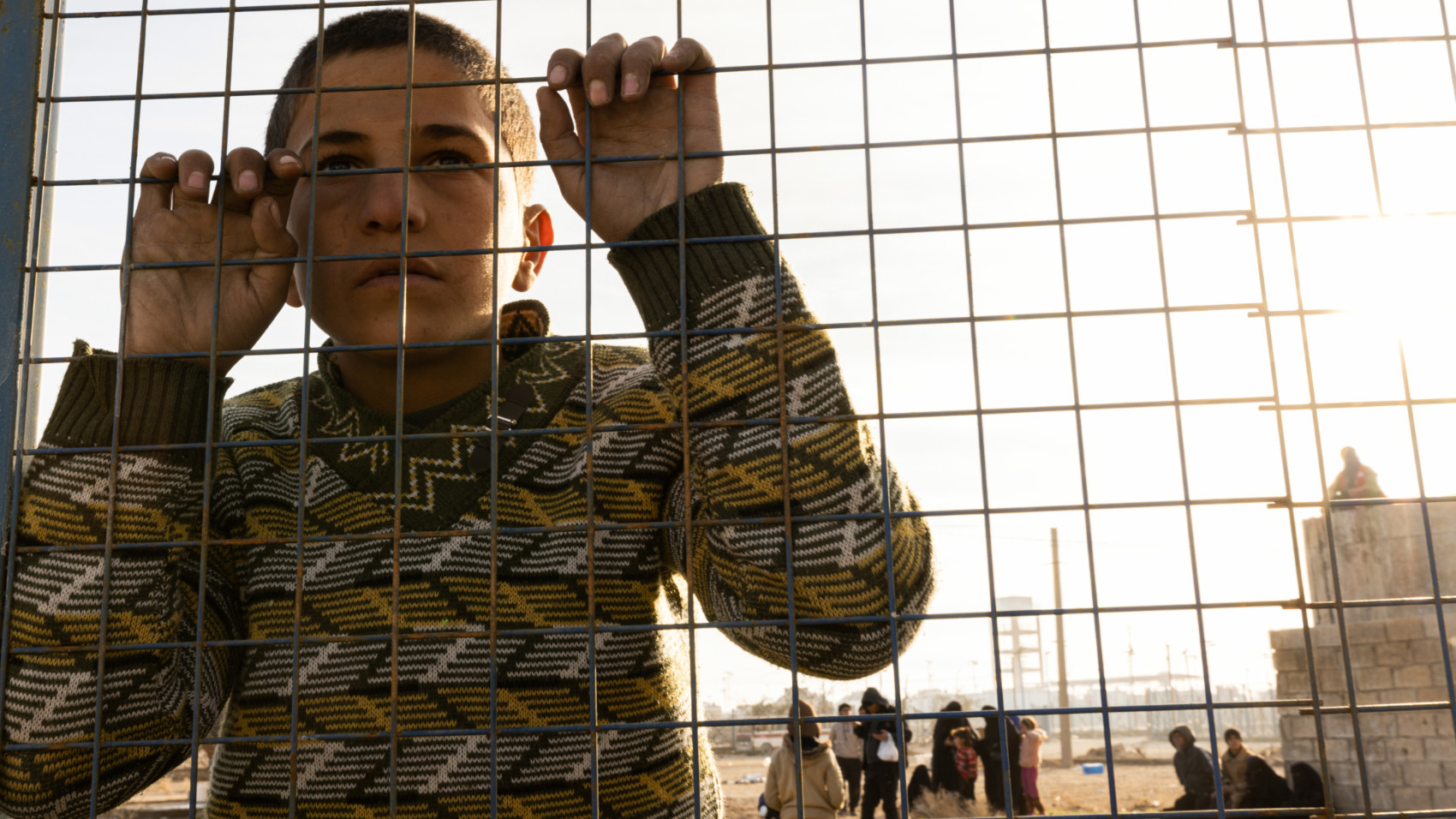 A child peers through barbed wire as soldiers move in and out of al-Hol camp in the Hasakeh countryside, Syria, 21 January 2026 (Hosam Katan/MEE)