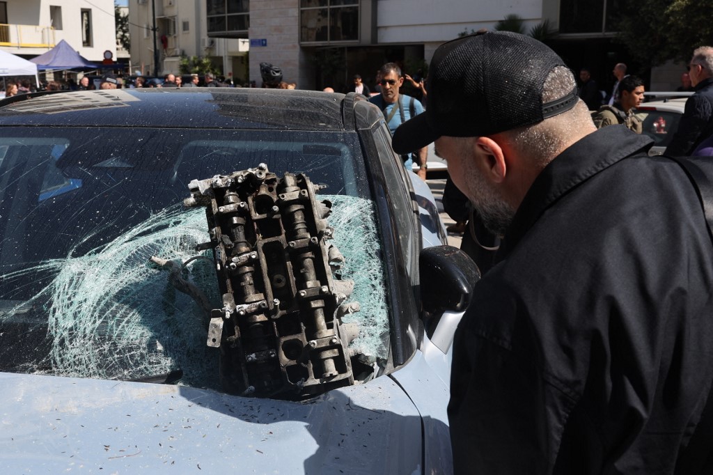 A man looks a part of a vehicle engine near the site of an Iranian missile strike in Tel Aviv on 24 March, 2026. (AFP)
