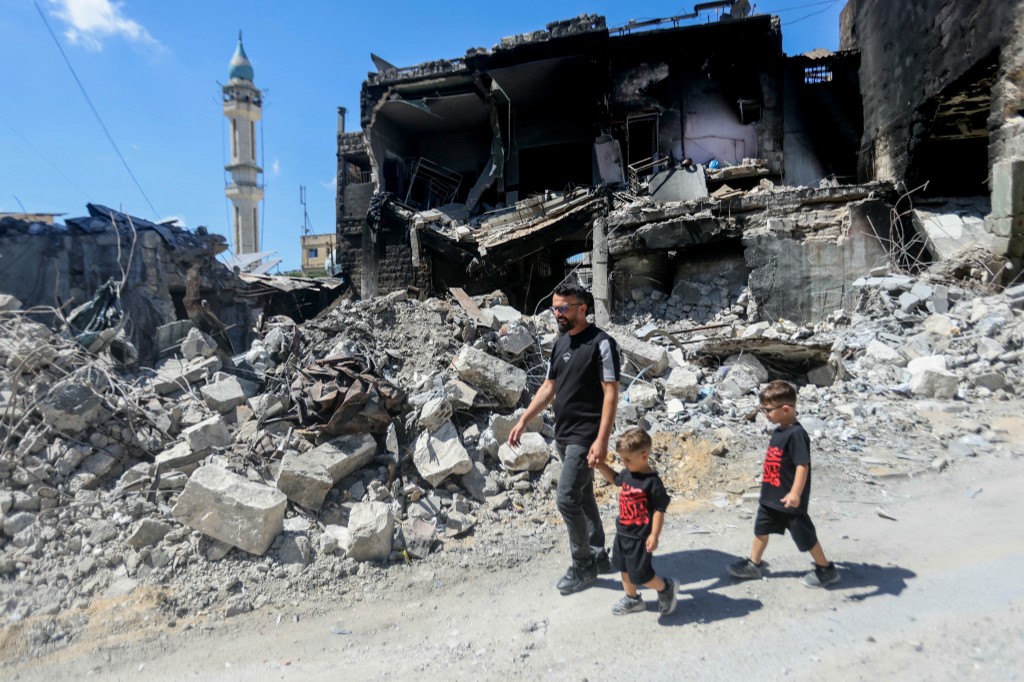 A man walks with his children past a destroyed building after returning to the southern Lebanese village of Nabatieh on June 18, 2026. 