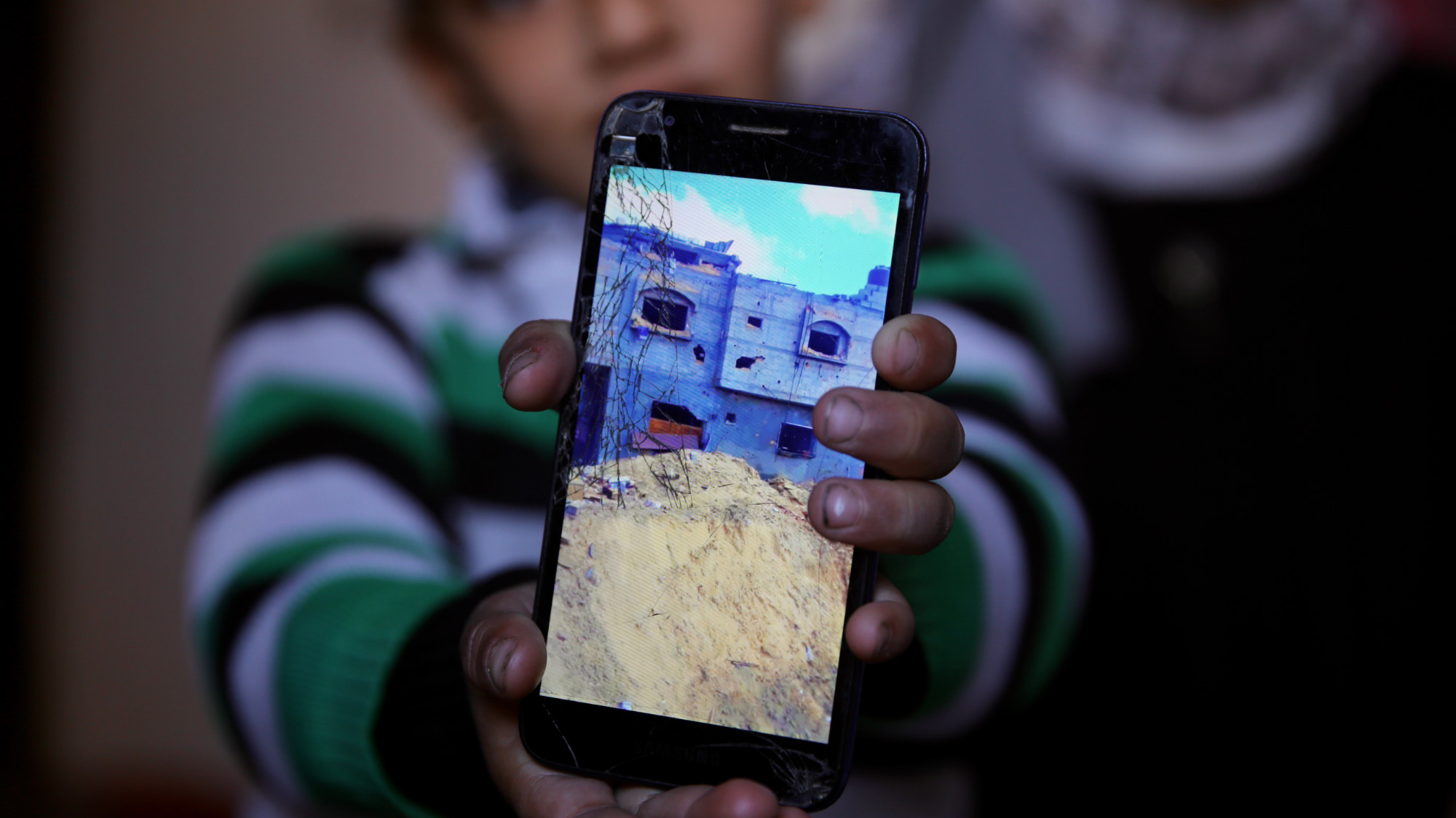 Sham al-Arian, xx's daughter, holds a phone showing a photo of the house were the dog attack took place in Khan Younis (MEE/Mohammed al-Hajjar) 