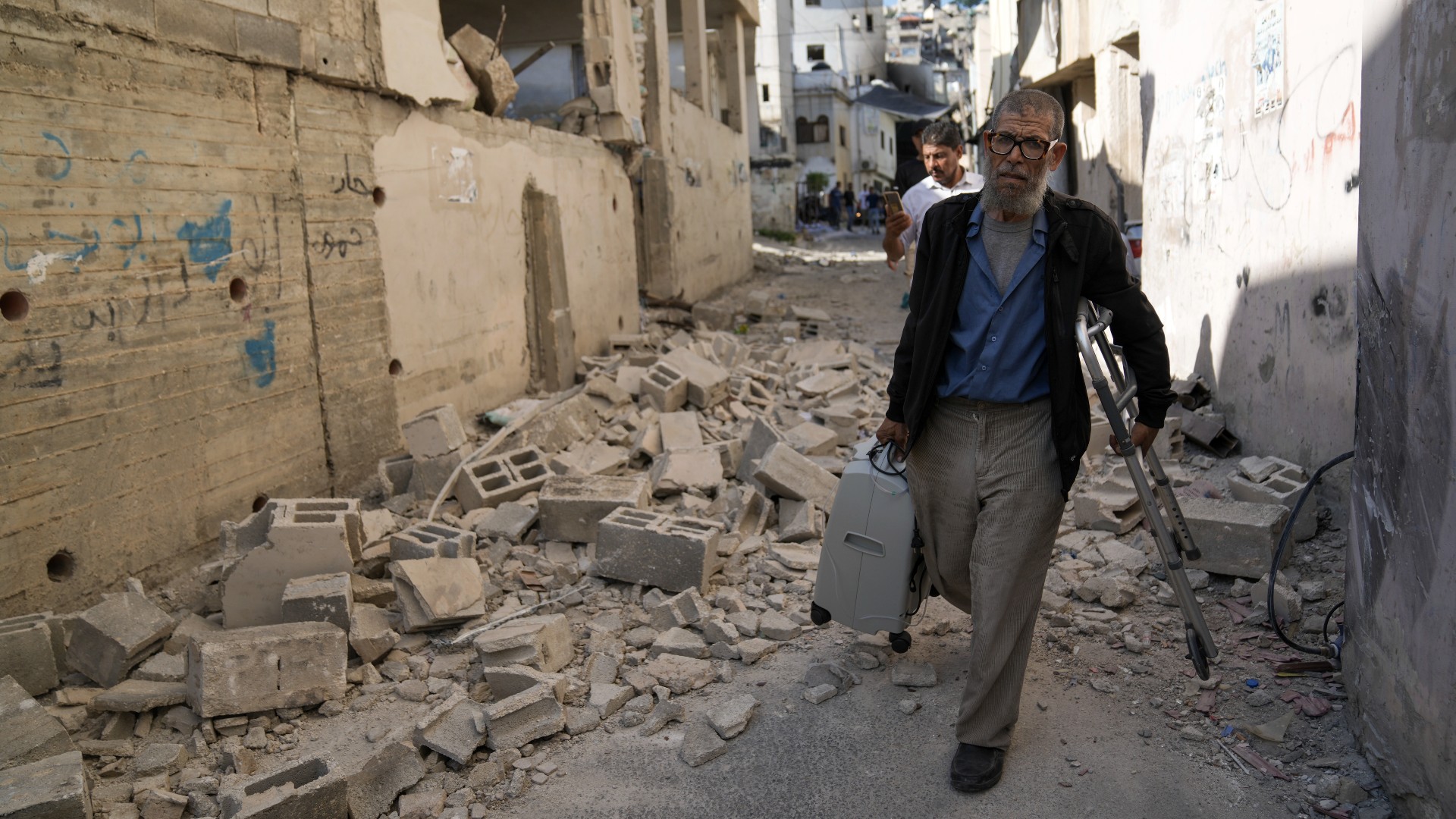 Palestinians walk by a damaged house in the Jenin refugee camp 5 July after the Israeli army withdrew its forces (AP)