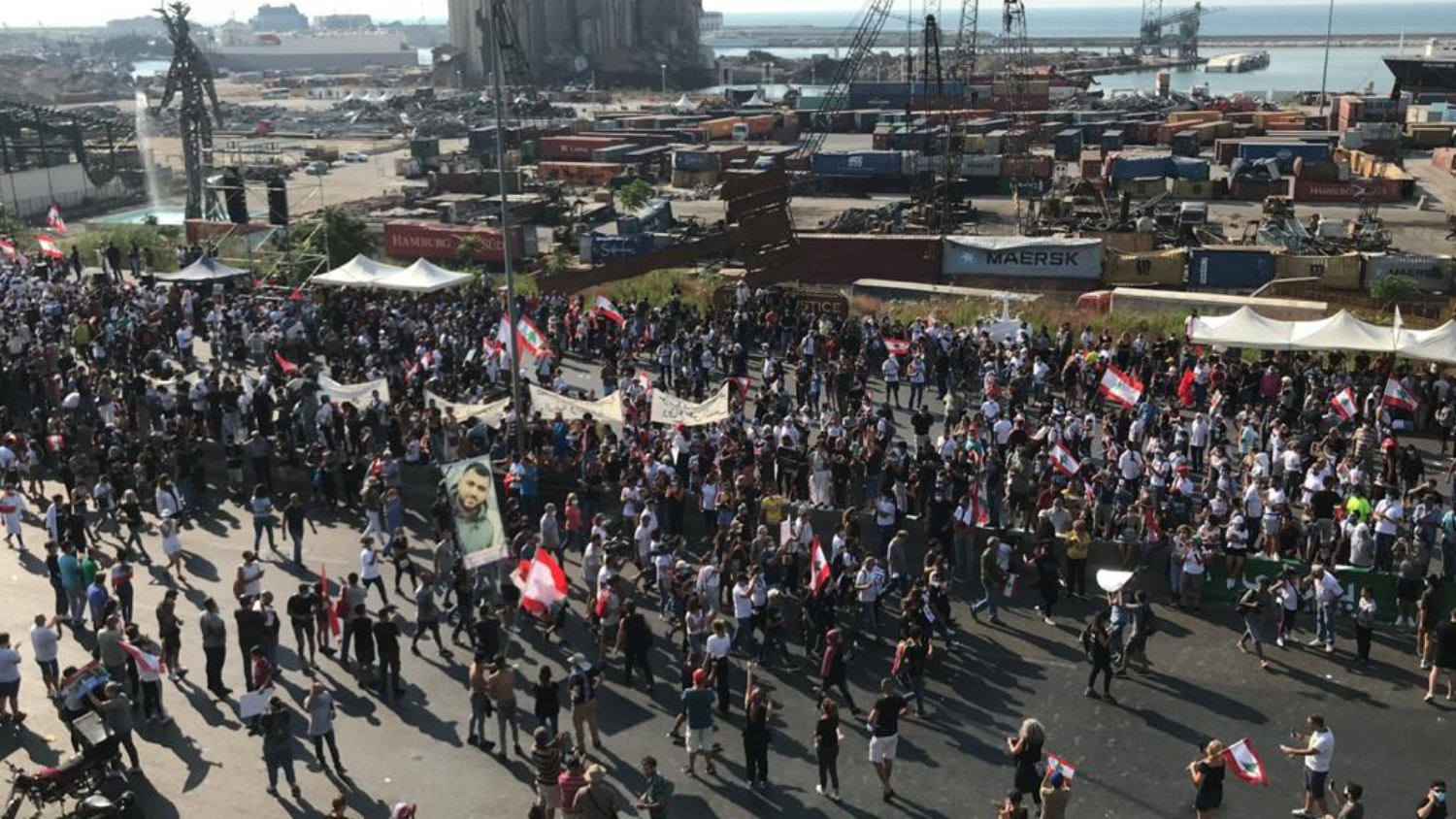 Protesters gather outside the Beirut port on 4 August 2021, holding photographs of victims of the explosion (MEE/Heba Nasser)