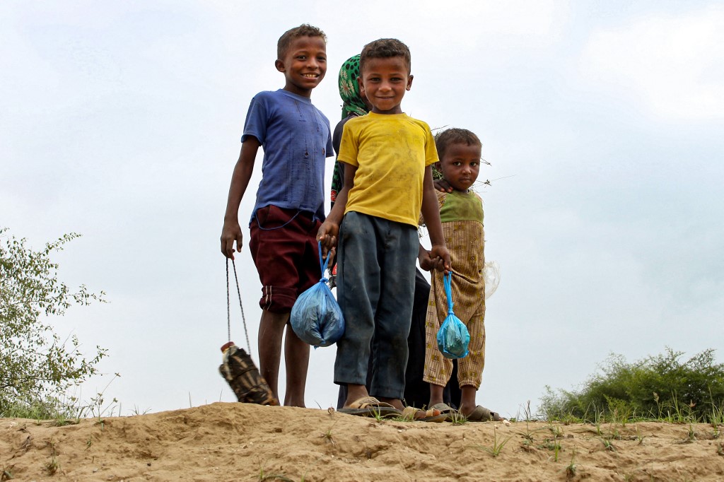 Children look on as they hold plastic bags and water bottles at a make-shift camp for displaced Yemenis in the northern Hajjah province on December 16, 2019 (AFP)