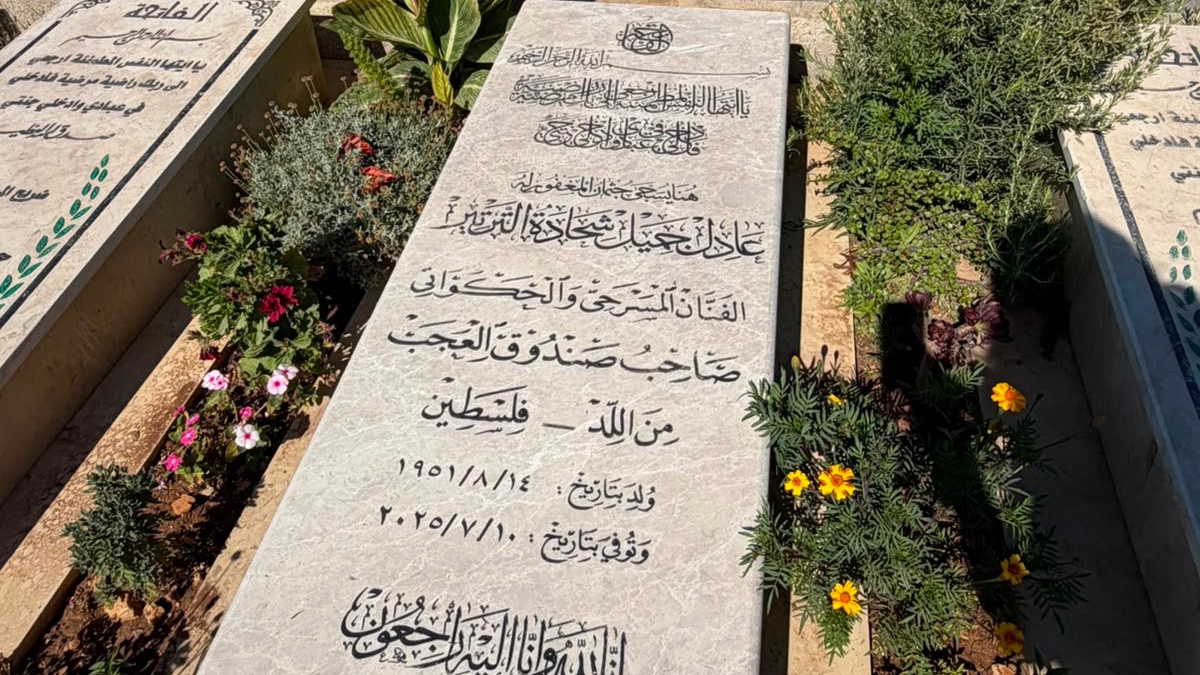 A marble headstone inscribed in Arabic, surrounded by flowers