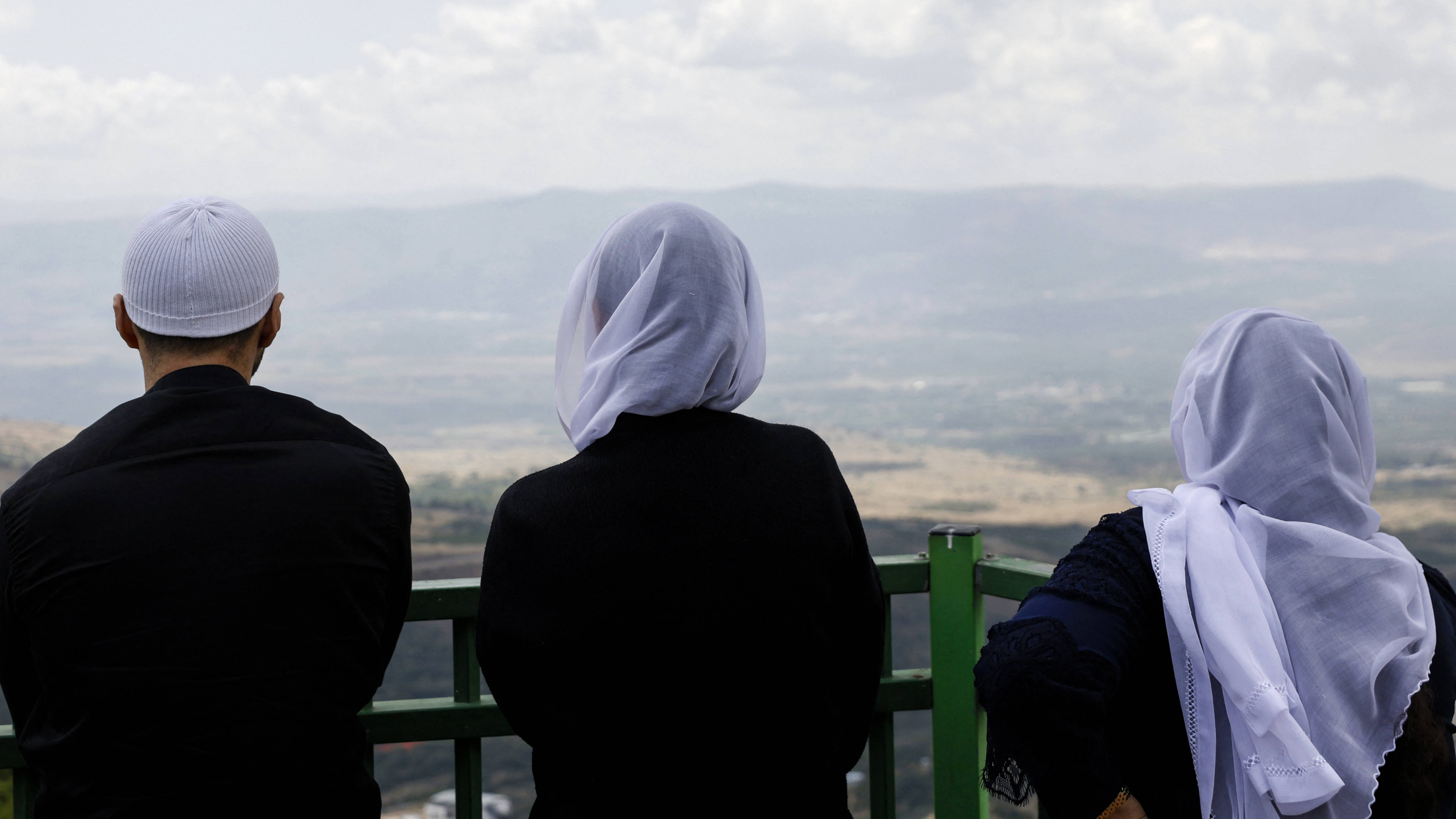 Members of a Druze family stare at the upper Galilee and southern Lebanese villages from a lookout in the Israeli-occupied Golan Heights on 25 May 2024 (AFP)