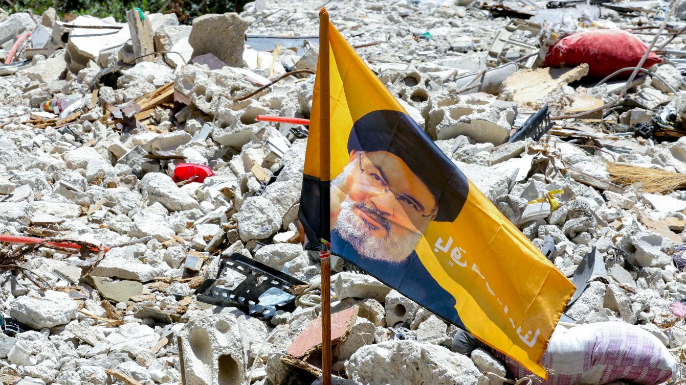 Flag bearing the image of slain Hezbollah leader Hassan Nasrallah stands amid rubble in Deir Qanoun al-Nahr, southern Lebanon, 16 June 2026 (Mahmoud Zayyat/AFP)