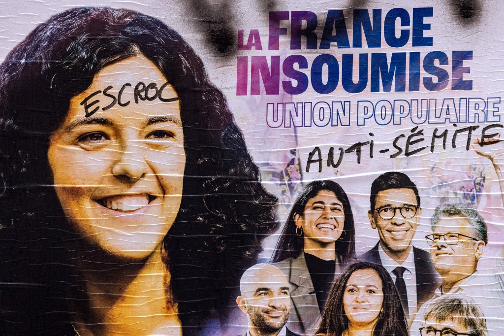 A European elections campaign poster of France Unbowed (LFI) with lead candidate Manon Aubry (on the left) and seventh candidate Rima Hassan (first on the right) with graffiti on it reading in French 