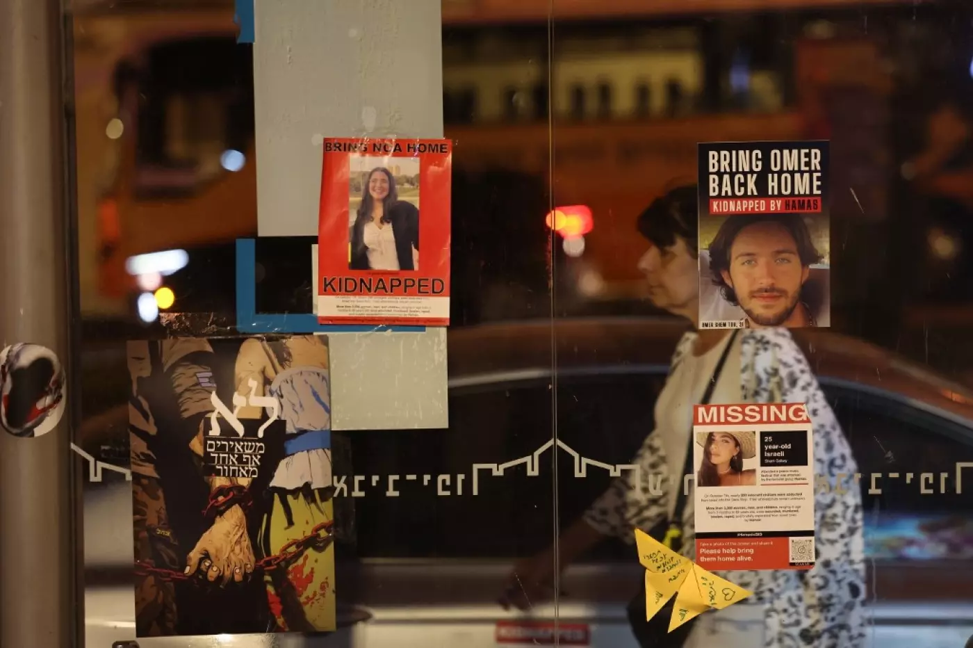 A woman walks past posters bearing the portraits of captives after a rally in Tel Aviv on 31 October (Ahmad Gharabli / AFP)