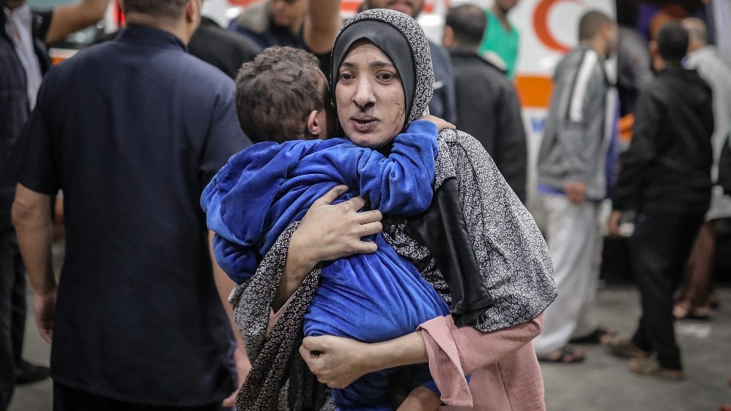 A woman covered in dust rushes with her child into the hospital after the Israeli bombardment of Khan Yunis in November 2023 (AFP/Belal Khaled)