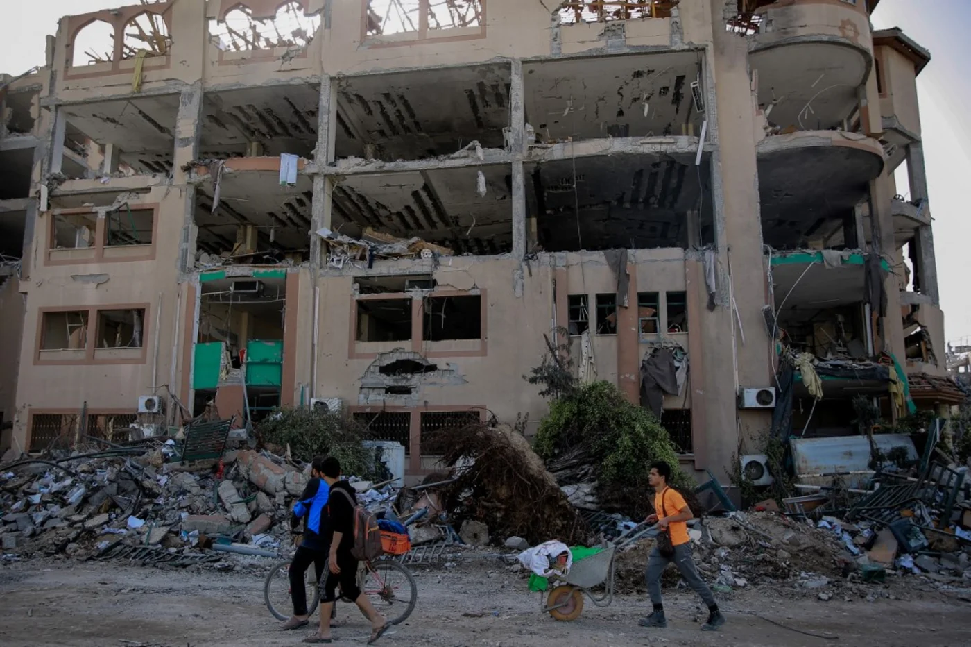 Palestinians walk past the destroyed building of the Islamic University in Gaza City on 26 November 2023 (Omar el-Qattaa/AFP)