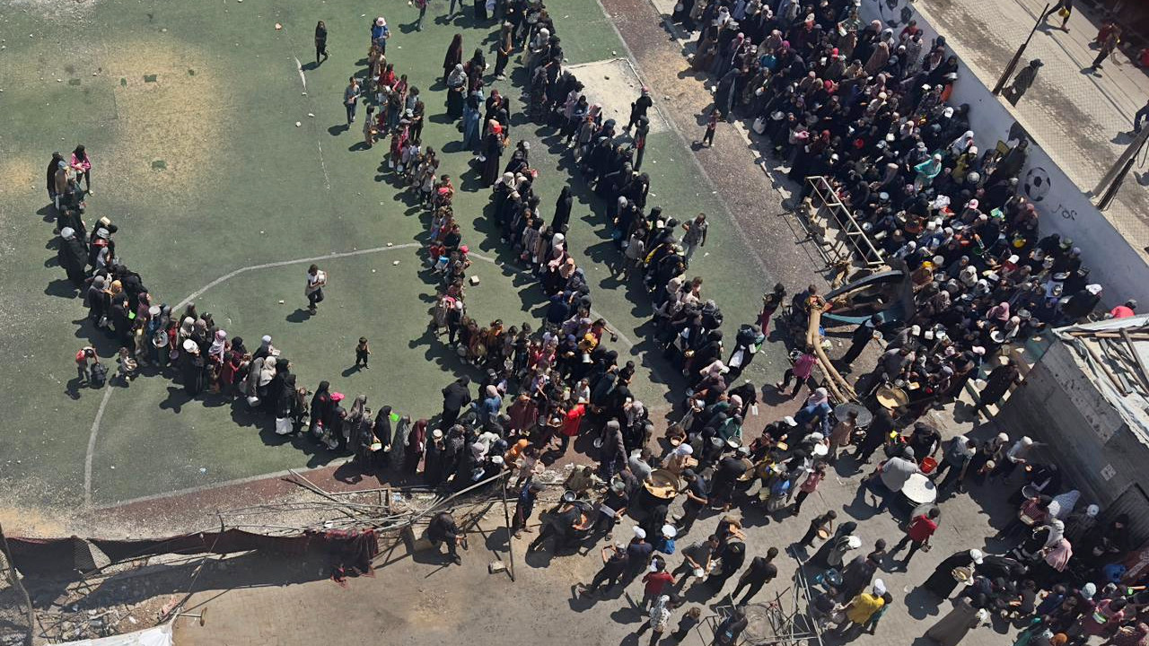 Palestinians in Gaza are seen lining up for hours in the scorching sun, desperate for a single ladle of food, in a photo captured by the author's friend Aya Nasser from her bedroom window in July 2025 (Supplied)
