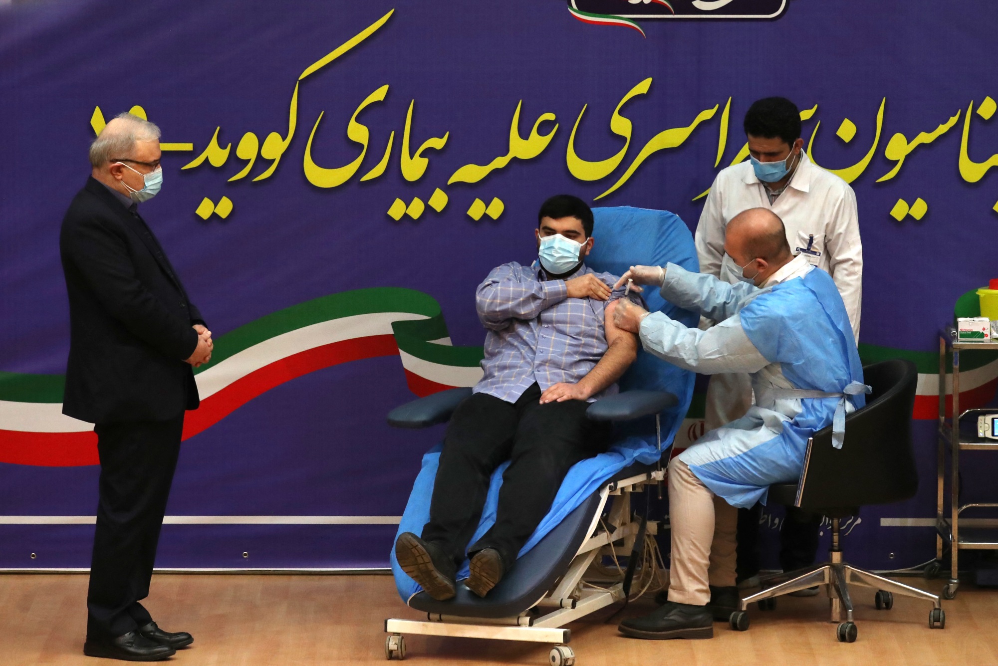 Iranian Health Minister Saeed Namaki watches while his son Parsa receives the first Covid-19 vaccine in the country on 9 February 2021 (AFP)