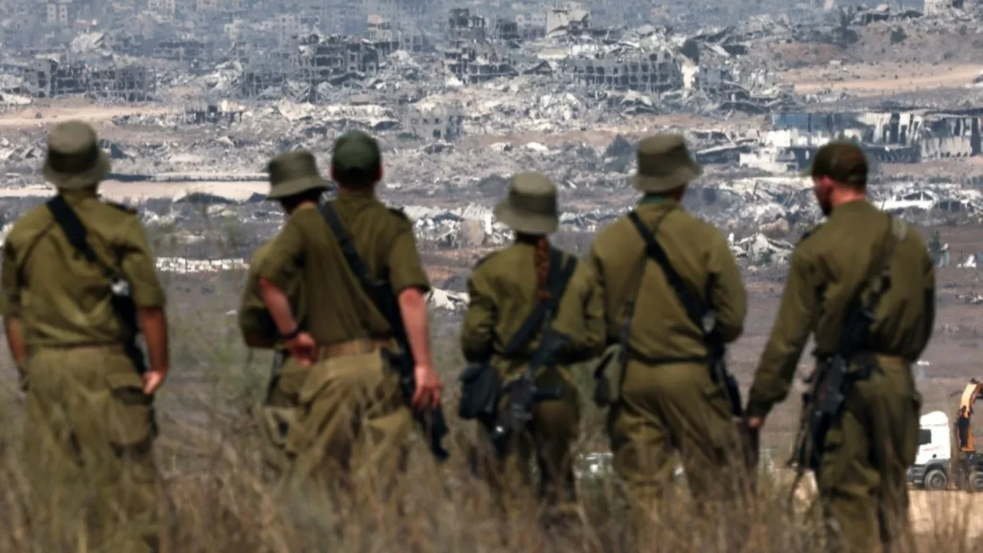 Israeli army soldiers look at destroyed buildings in the Gaza Strip as they stand at the boundary of the Palestinian territory on 13 August