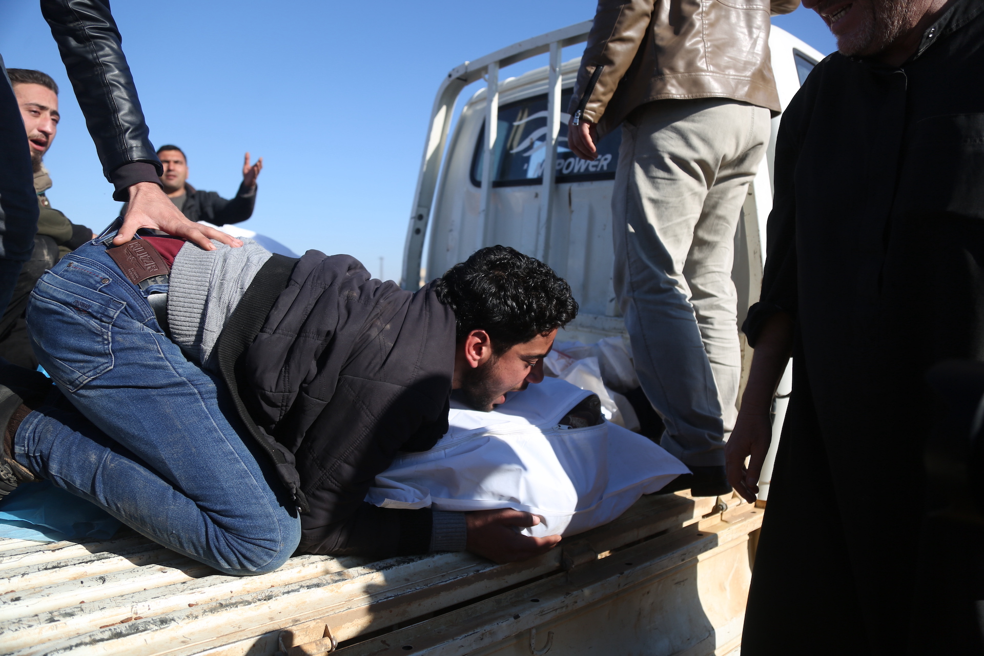 A relative of the slain family members clutches at one of the remains prepared for burial in Maarat al-Naasan on 12 February (MEE/Ali Haj Suleiman)