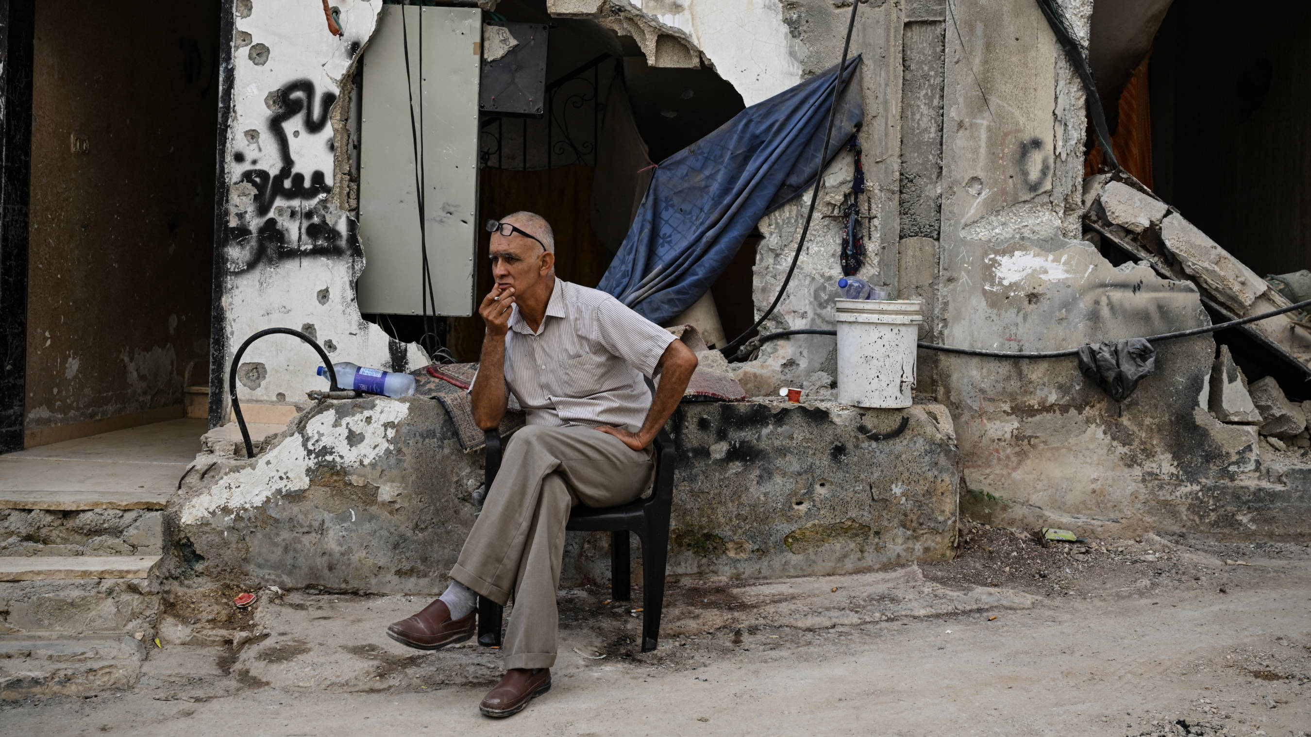A man sits in front of a damaged building following an Israeli military raid in the Jenin refugee camp, occupied West Bank, on 6 September 2024 (Ronaldo Schemidt / AFP)