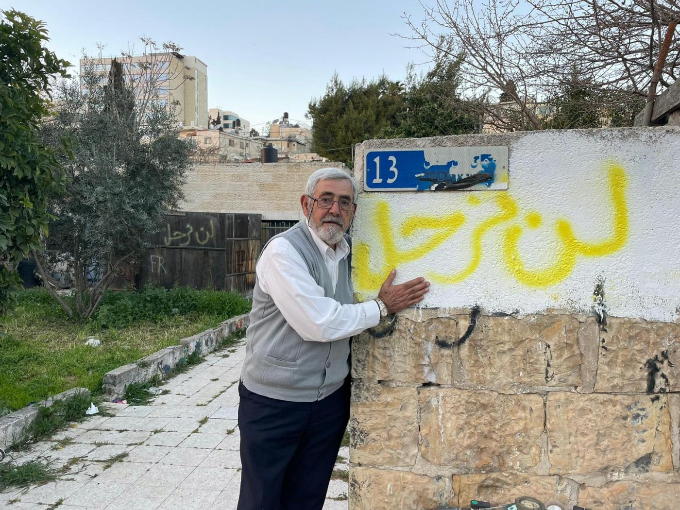 Nabil al-Kurd, a long-time resident of Karm al-Jaouni, stands next to a wall graffitied with “We will not leave” in Arabic (MEE/Aseel Jundi)