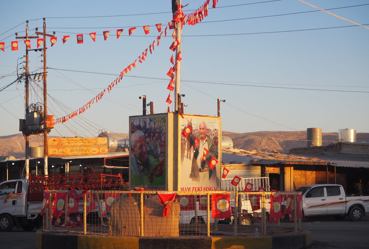 Bunting for the Pade party hangs from a roundabout in the centre of Sinouni, around posters commemorating a YBS commander killed by a Turkish airstrike in 2018 (MEE correspondent)