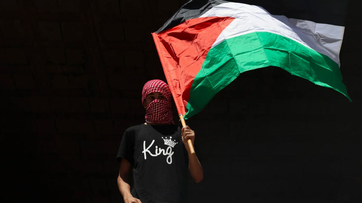 A man carries a flag of Palestine during the funeral of Hamdan Abu Alia, 18, who was killed in an Israeli raid in al-Mughayyir village, in Ramallah in the occupied West Bank on 17 August 2025 (Zain Jaafar/AFP)