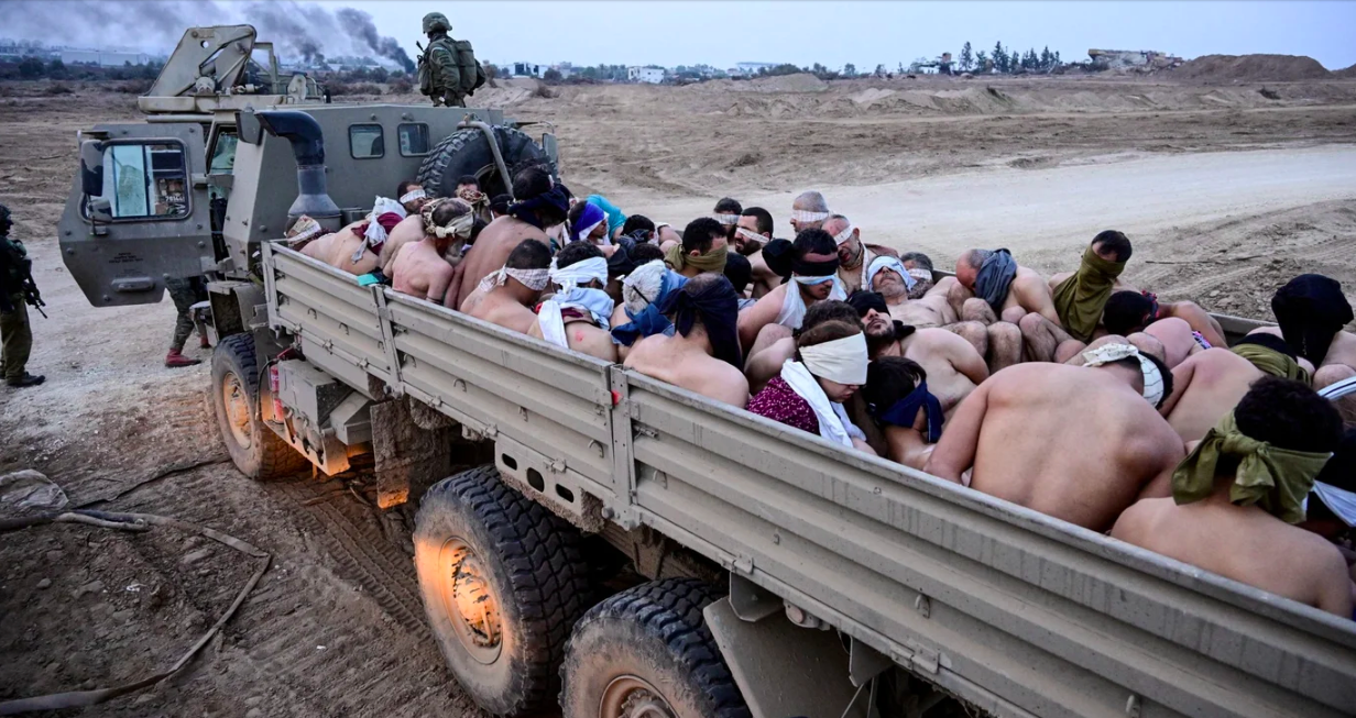 Israeli soldiers stand by a truck packed with shirtless Palestinian men and one woman in the besieged Gaza Strip on 8 December 2023 (Reuters/Yossi Zeliger)