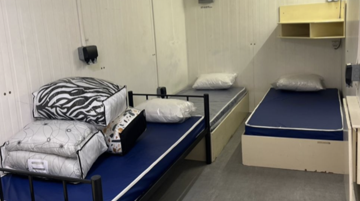 A sparse, cramped, and windowless room is shown inside a container for residents of Camp As Sayliyah in Qatar